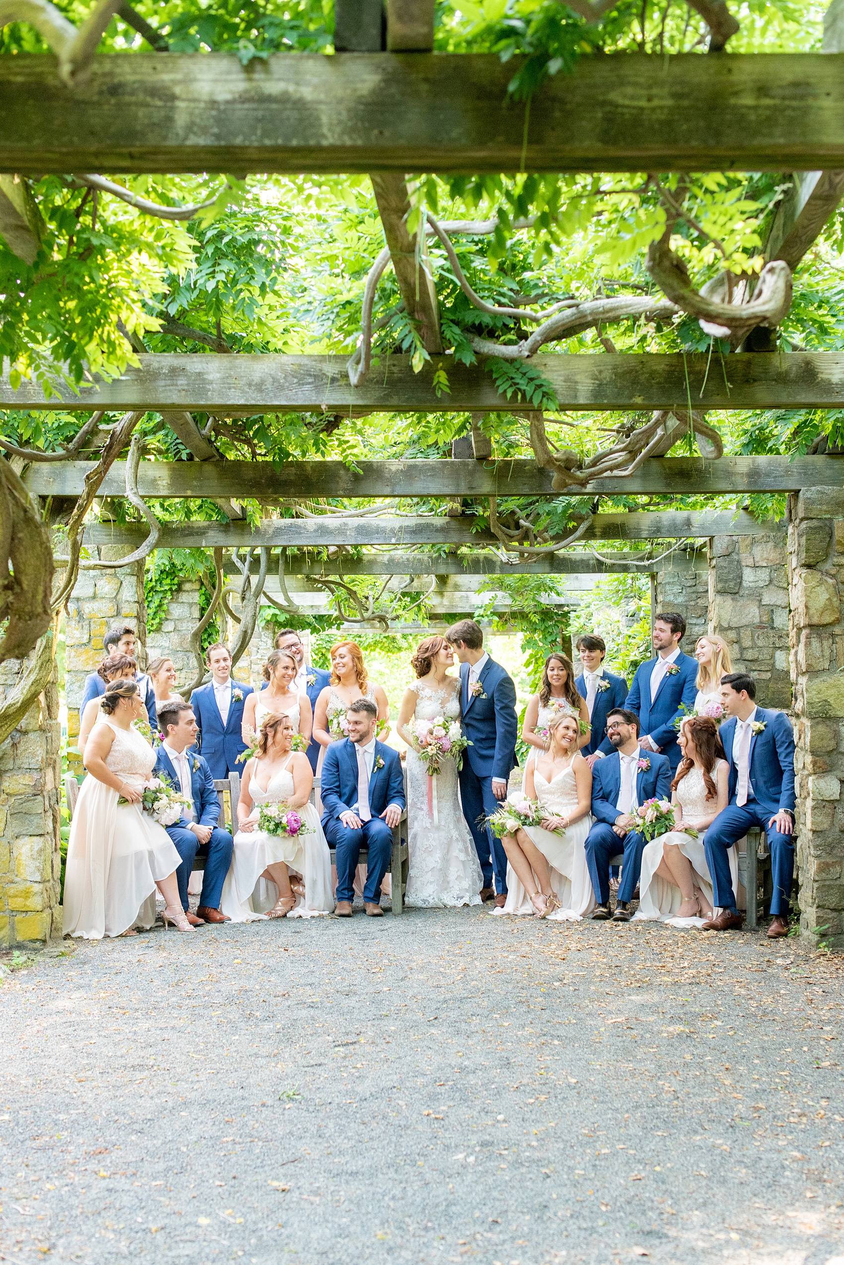 A summer wedding at Olde Mill Inn, NJ. Photos by Mikkel Paige Photography. This New Jersey venue is a great option for an event not too far from NYC. The wedding party photos were at nearby Cross Estate Gardens, a beautiful lush area for bridal party and groomsmen photos. The bridesmaids wore light pink, mis-matched gowns and the guys wore blue suits with pink ties in this unique, Vogue-like picture. Click through for their complete wedding recap! #OldeMillInn #NJwedding #NJweddingphotographer #mikkelpaige #NewJerseyWeddingVenue #NewJerseyWedding #CrossEstateGardens #weddingdetails #bridalparty #pinkbridesmaids #mismatcheddresses #bluesuits #groomsmen