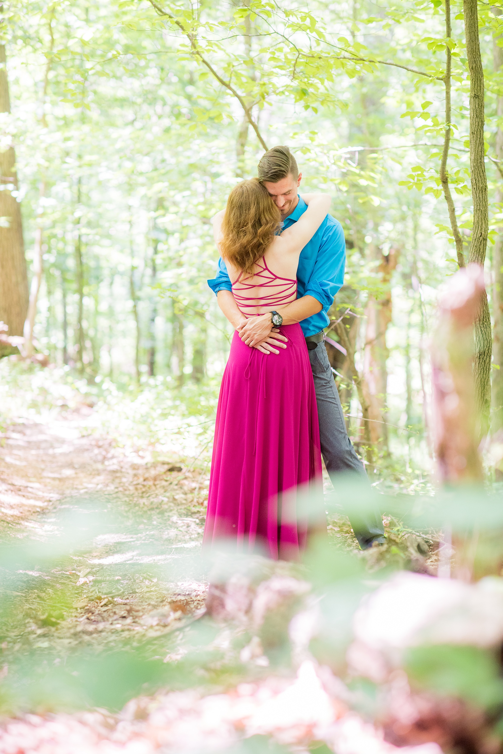 Maryland summer engagement photos by Mikkel Paige Photography. This couple wore semi-formal outfits with the bride in a beautiful, sexy back fuchsia pink gown and the groom in a blue button down and grey pants. Their elegant outdoor park pictures were perfect for the season! Click through to see more from their romantic pictures in the woods! #mikkelpaige #summerengagementphotos #marylandengagementphotos #marylandweddingphotographer #parkengagementsession #engagementphotooutfitideas #engagementphotos #savethedatephotos 