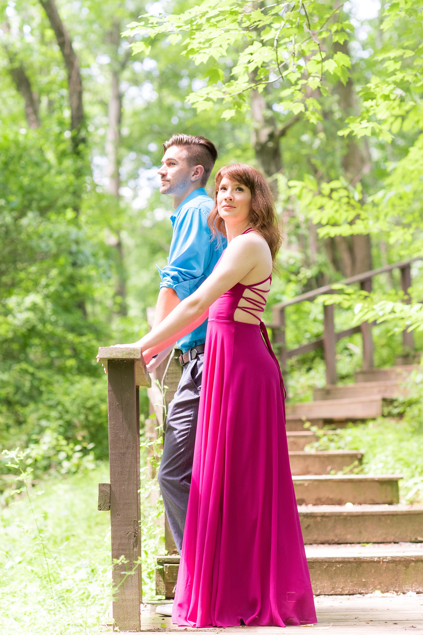 Maryland summer engagement photos by Mikkel Paige Photography. This couple wore semi-formal outfits with the bride in a beautiful, sexy back fuchsia pink gown and the groom in a blue button down and grey pants. Their elegant outdoor park pictures were perfect for the season! Click through to see more from their romantic pictures in the woods! #mikkelpaige #summerengagementphotos #marylandengagementphotos #marylandweddingphotographer #parkengagementsession #engagementphotooutfitideas #engagementphotos #savethedatephotos 