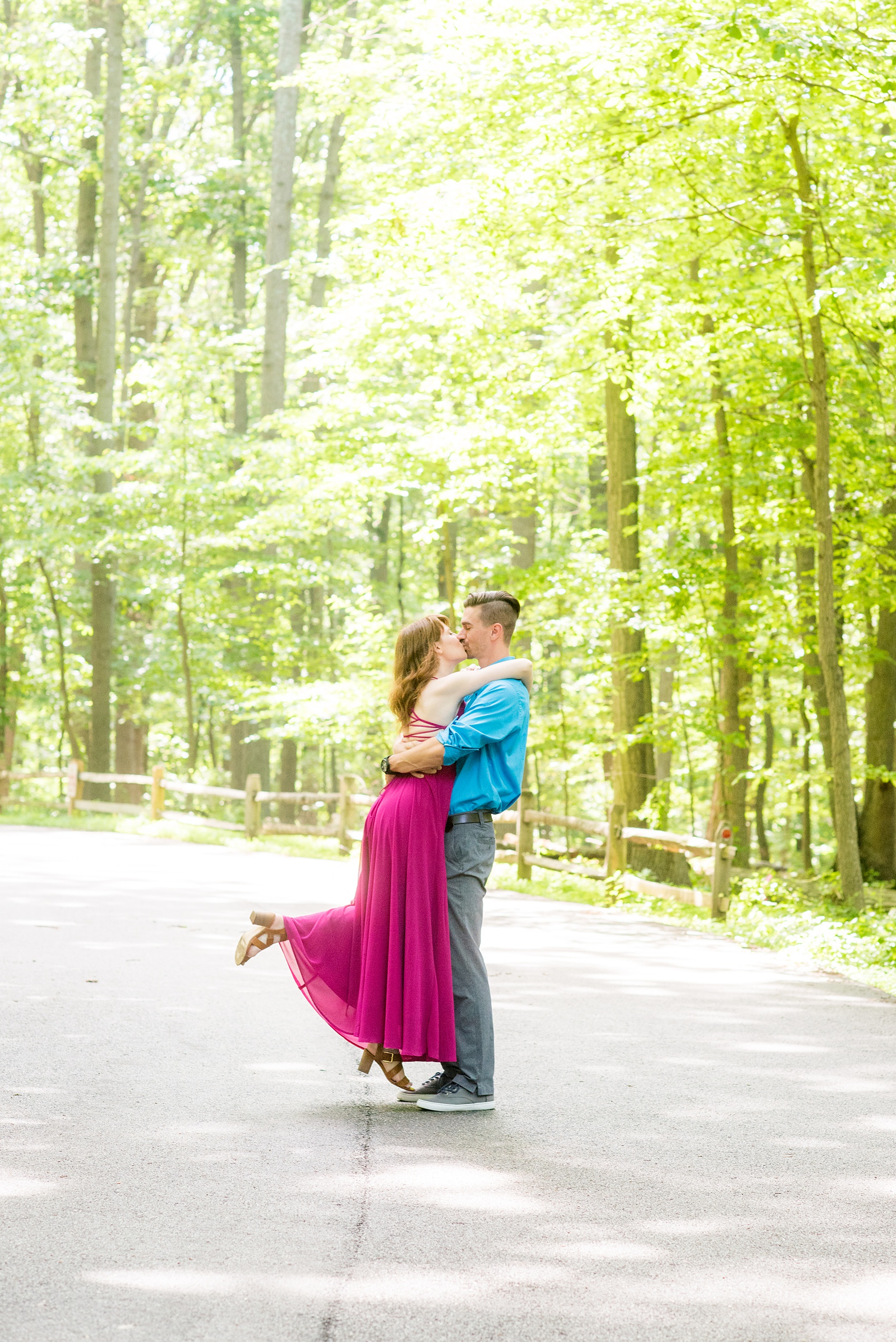 Maryland summer engagement photos by Mikkel Paige Photography. This couple wore semi-formal outfits with the bride in a beautiful, sexy back fuchsia pink gown and the groom in a blue button down and grey pants. Their elegant outdoor park pictures were perfect for the season! Click through to see more from their romantic pictures in the woods! #mikkelpaige #summerengagementphotos #marylandengagementphotos #marylandweddingphotographer #parkengagementsession #engagementphotooutfitideas #engagementphotos #savethedatephotos 