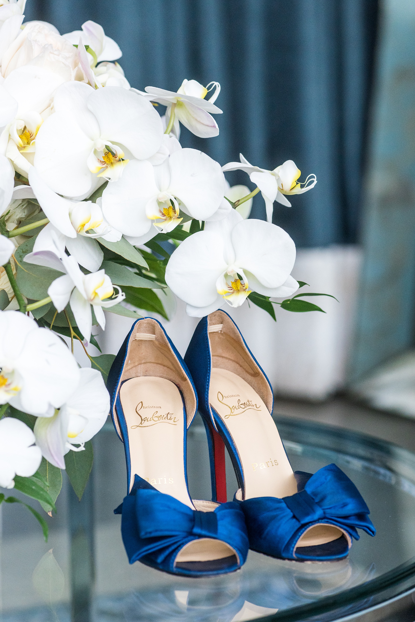 Downtown Raleigh wedding venue photos of Vidrio on Glenwood South, and their beautiful new bridal suite. Glass tables and colorful rugs are the perfect place to photograph details like a pair of vibrant, navy blue Christian Louboutin wedding shoes. #MikkelPaige #Vidrio #DowntownRaleigh #RaleighWeddingVenues #weddingdetails #blueshoes #whiteorchids #somethingblue #christianlouboutin