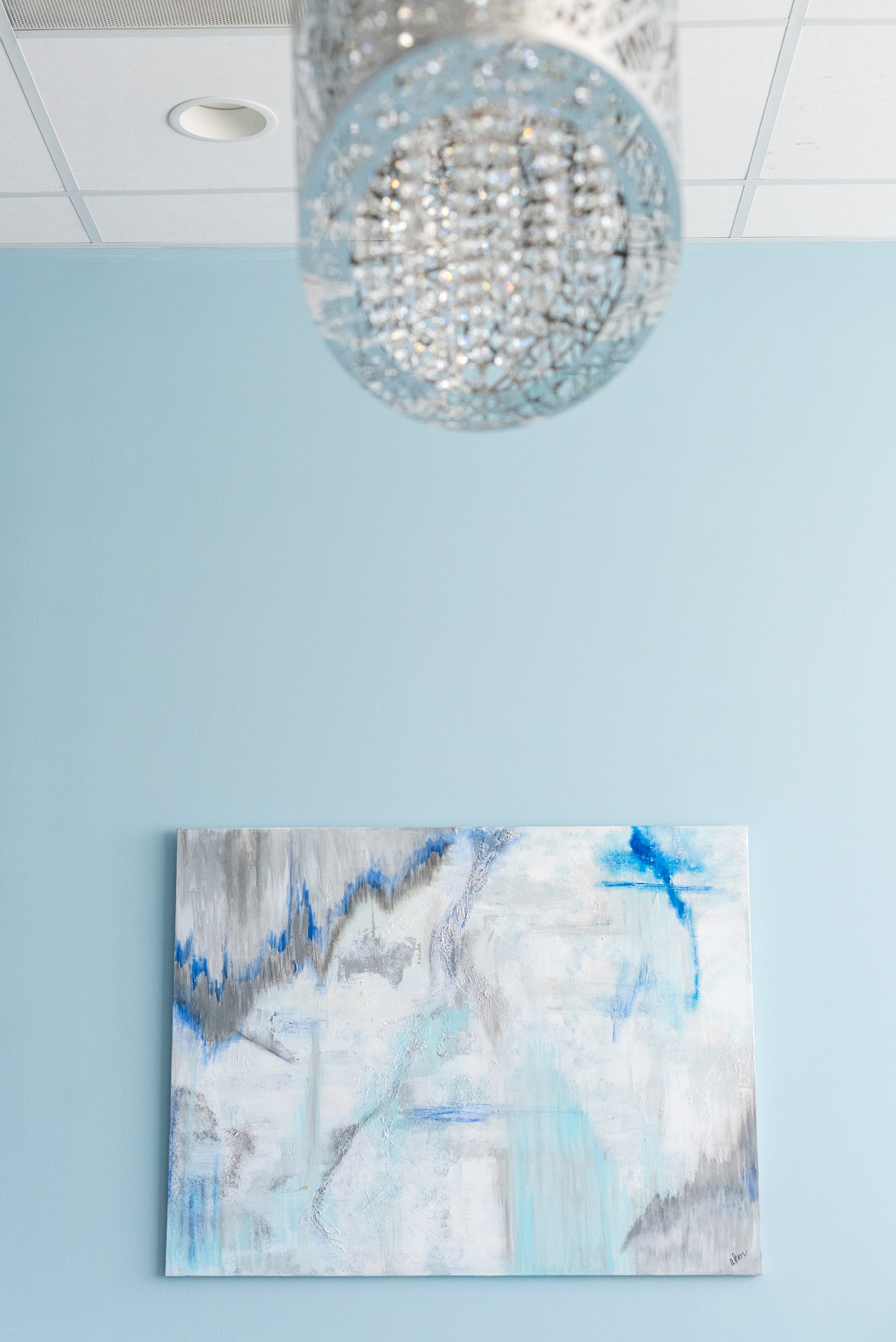 Downtown Raleigh wedding venue photos of Vidrio on Glenwood South, and their beautiful new bridal suite. Blue hues and neutral furniture are framed by paintings and a chandelier light fixture in this pretty space. #MikkelPaige #Vidrio #DowntownRaleigh #RaleighWeddingVenues