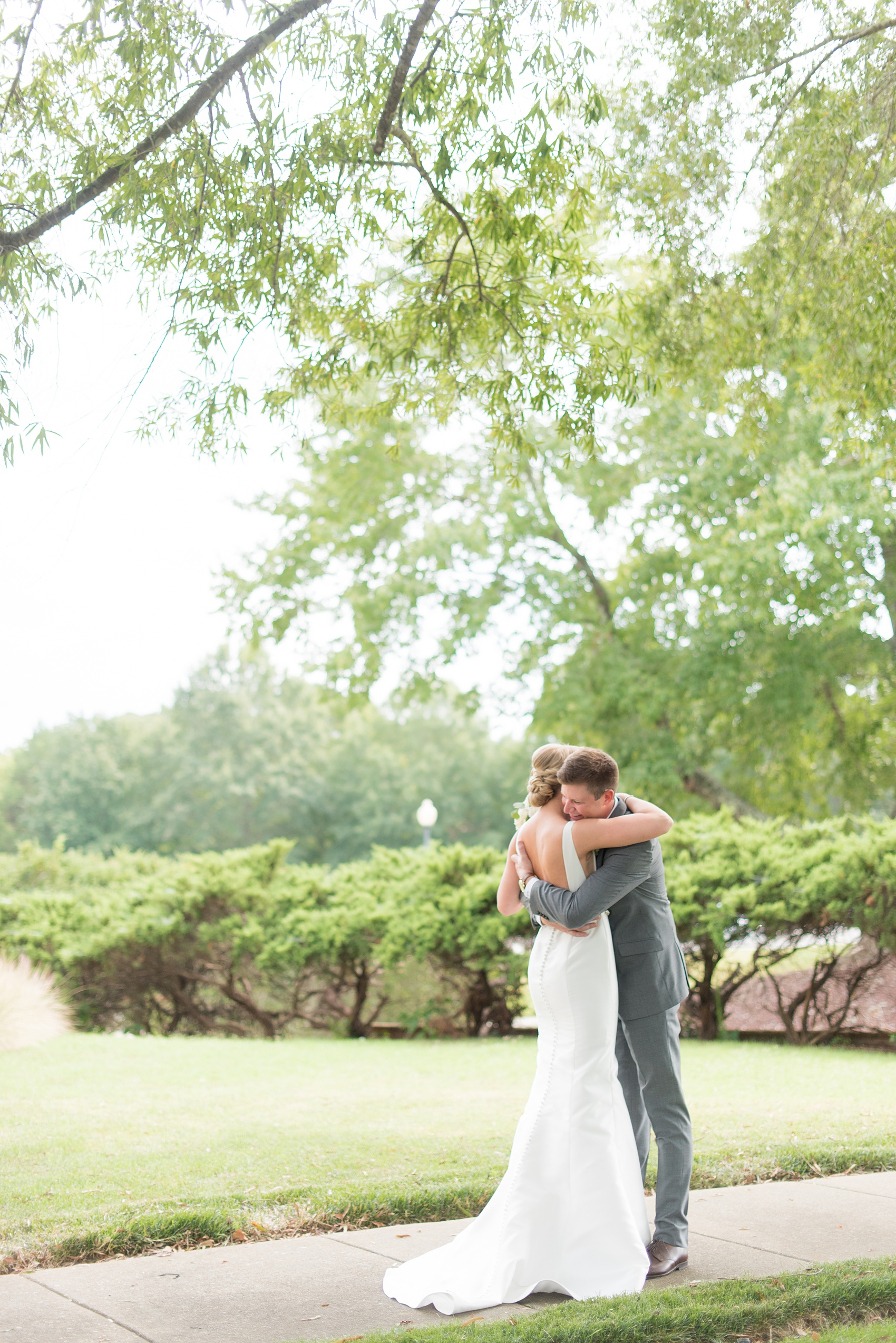 Pictures by Mikkel Paige Photography of a wedding in Durham, North Carolina. The bride carried hydrangea flowers for the garden-like golf course photos with her groom, who wore a grey suit. Her low-back gown and up-do hair twists were beautiful! Click through to the website post for complete details and more inspiration! #durhamNC #northcarolinawedding #golfcoursewedding #CountryClub #DurhamWedding #summerwedding #weddinggown #lowbackweddinggown #brideandgroom #firstlook