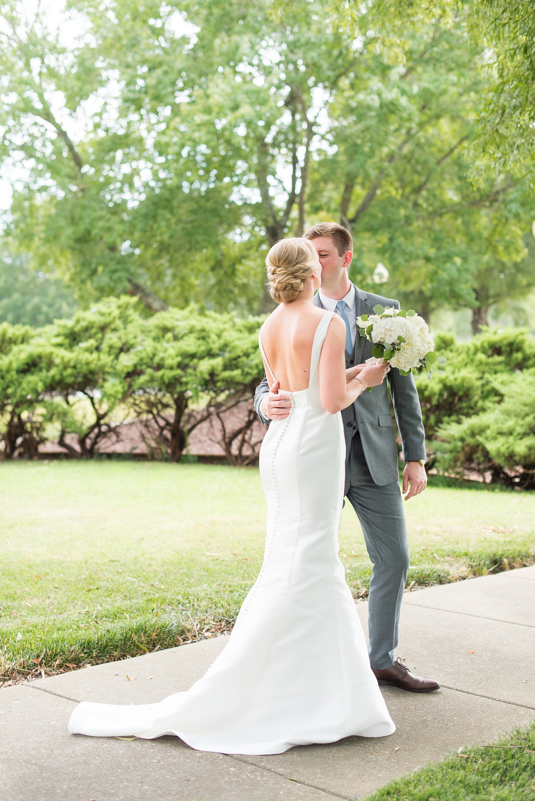 Pictures by Mikkel Paige Photography of a wedding in Durham, North Carolina. The bride carried hydrangea flowers for the garden-like golf course photos with her groom, who wore a grey suit. Her low-back gown and up-do hair twists were beautiful! Click through to the website post for complete details and more inspiration! #durhamNC #northcarolinawedding #golfcoursewedding #CountryClub #DurhamWedding #summerwedding #weddinggown #lowbackweddinggown #brideandgroom #firstlook