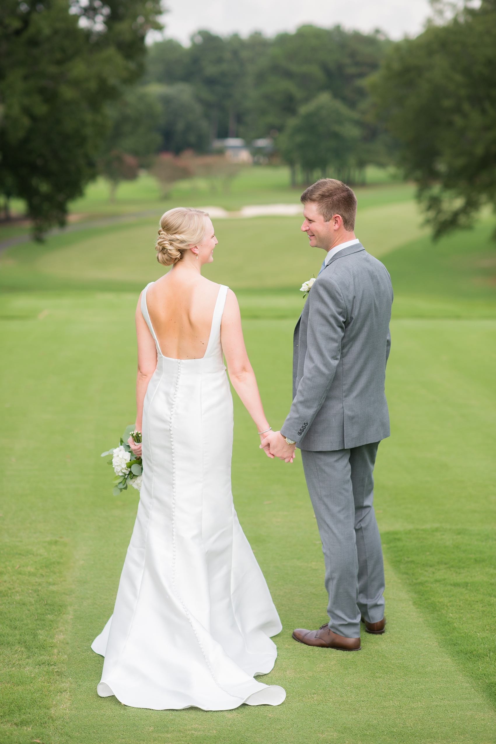 Pictures by Mikkel Paige Photography of a wedding in Durham, North Carolina. The bride carried hydrangea flowers for the garden-like golf course photos with her groom, who wore a grey suit. Her low-back gown and up-do hair twists were beautiful! Click through to the website post for complete details and more inspiration! #durhamNC #northcarolinawedding #golfcoursewedding #CountryClub #DurhamWedding #summerwedding #weddinggown #lowbackweddinggown #brideandgroom