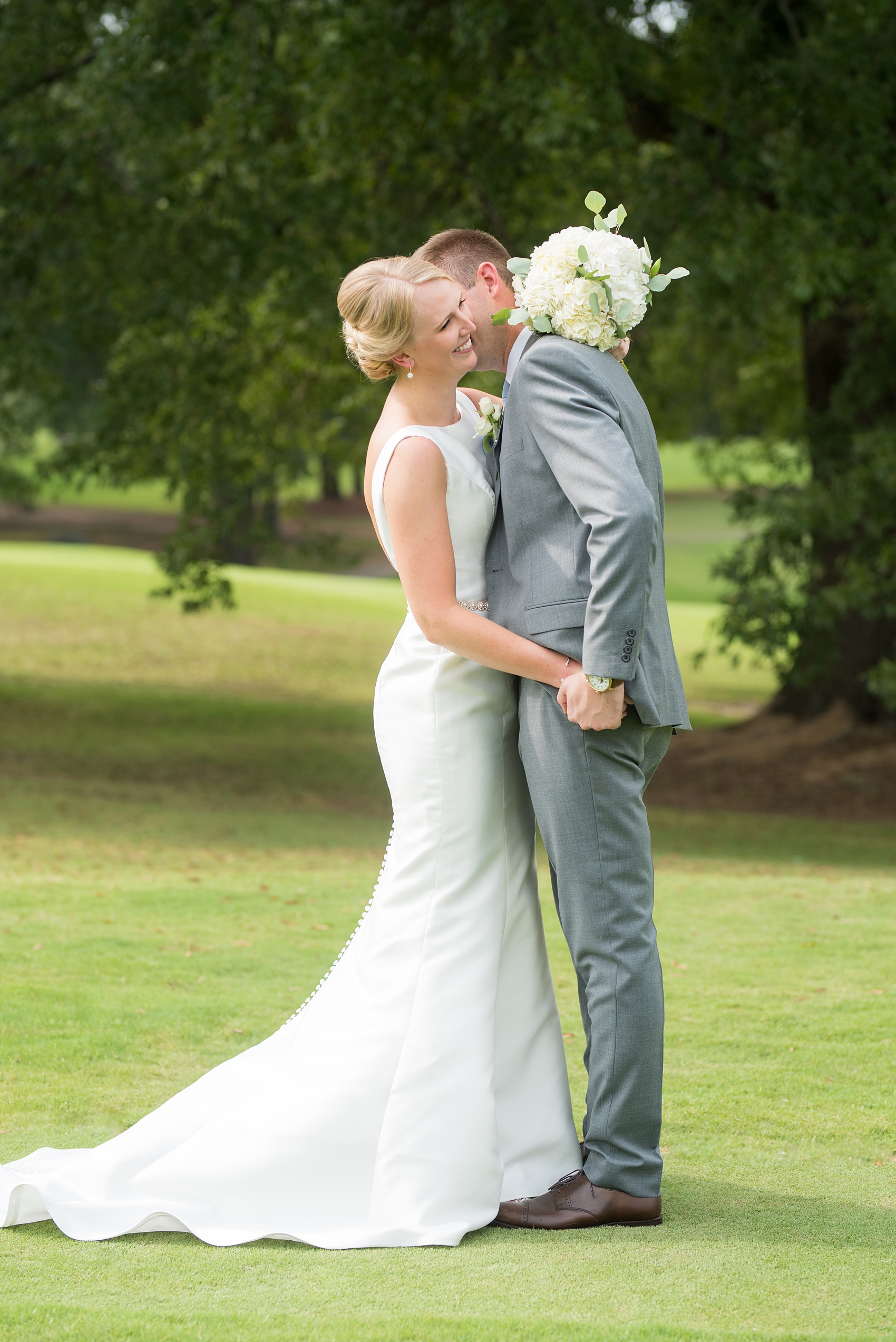 Pictures by Mikkel Paige Photography of a wedding in Durham, North Carolina. The bride carried hydrangea flowers for the garden-like golf course photos with her groom, who wore a grey suit. Her low-back gown and up-do hair twists were beautiful! Click through to the website post for complete details and more inspiration! #durhamNC #northcarolinawedding #golfcoursewedding #CountryClub #DurhamWedding #summerwedding #weddinggown #lowbackweddinggown #brideandgroom