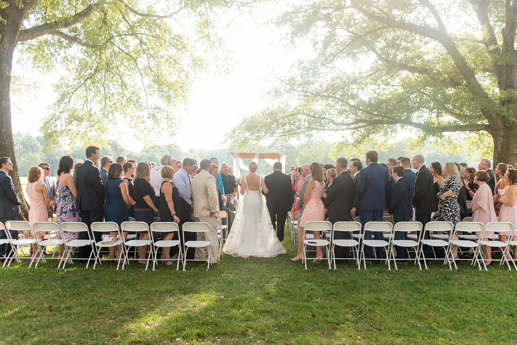 Pictures by Mikkel Paige Photography of a wedding in Durham, North Carolina. The bride and groom stood under a simple arch during their outdoor ceremony at Croasdaile Country Club, a golf-course venue with beautiful gardens and towering oak trees.Click through to our website for endless ideas and the complete post! #durhamNC #northcarolinawedding #golfcoursewedding #CountryClubWedding #bluebridesmaids #DurhamWedding #summerwedding #southernwedding #outdoorceremony #goldenhourceremony