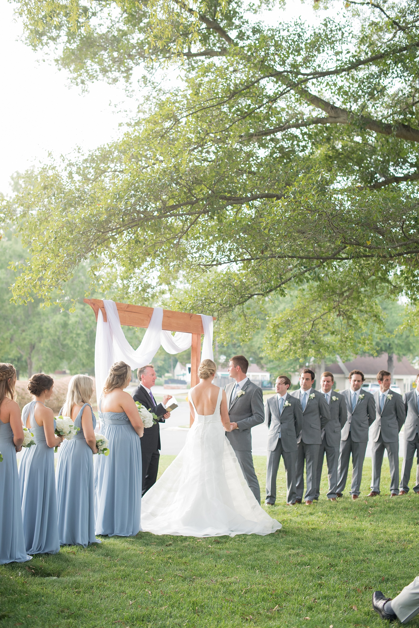 Pictures by Mikkel Paige Photography of a wedding in Durham, North Carolina. The bride and groom stood under a simple arch during their outdoor ceremony at Croasdaile Country Club, a golf-course venue with beautiful gardens and towering oak trees.Click through to our website for endless ideas and the complete post! #durhamNC #northcarolinawedding #golfcoursewedding #CountryClubWedding #bluebridesmaids #DurhamWedding #summerwedding #southernwedding #outdoorceremony #goldenhourceremony