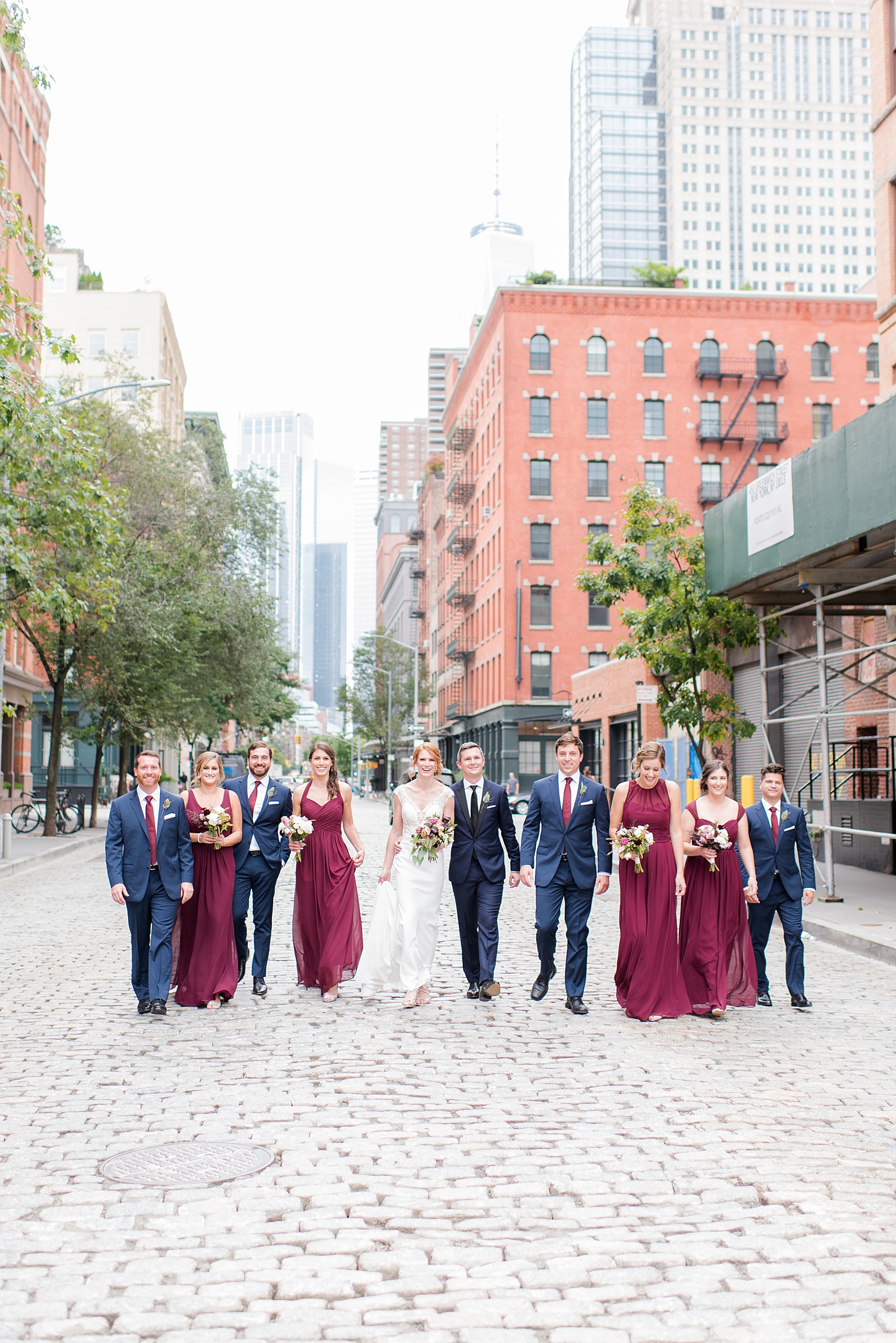 Wedding photos at Tribeca Rooftop by Mikkel Paige Photography, in NYC. This Manhattan venue has the perfect view of the New York City skyline including Freedom Tower. The bridal party walked along the cobblestone streets in the city for this fun photo. #ManhattanWedding #TribecaRooftop #TribecaRooftopWeddingPhotos #SeptemberWedding #Groom #MikkelPaige #WeddingPhotos #Groomsmen #BridalParty #cobblestoneweddingphotos #RedBridesmaids #CranberryBridesmaids #RedWeddingInspiration #BerryWeddingInspiration
