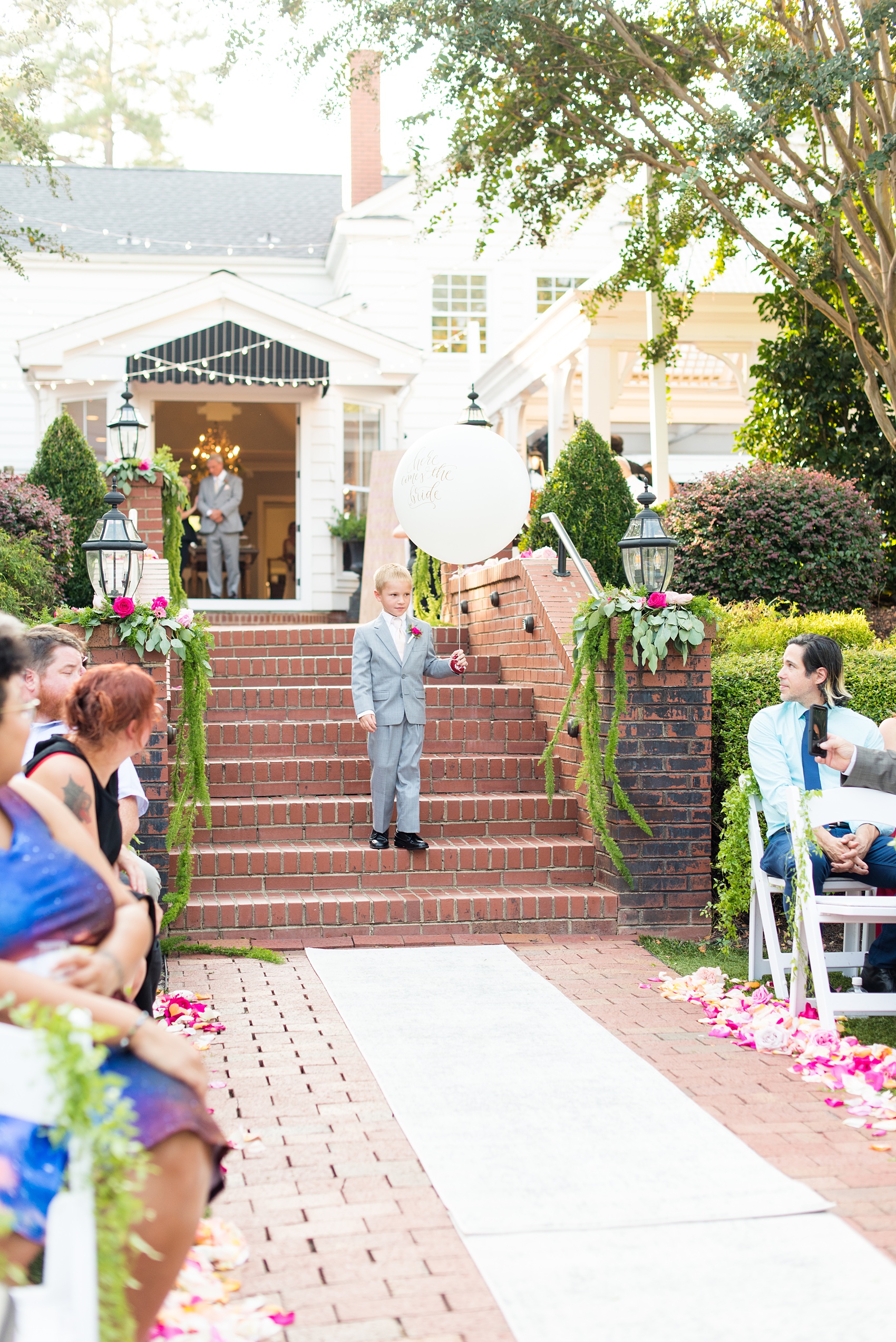 Highgrove Estate wedding photos by Mikkel Paige Photography. It’s a beautiful venue for a wedding large or small, near Raleigh, North Carolina. This wedding had fun signs, custom stationery and table numbers that said places the bride & groom travel to, and romantic candlelight planned by @asouthernsoiree. Click through to see the tropical green leaves, pink and orange flowers dripping from their outdoor ceremony space! #NorthCarolinaVenues #MikkelPaige #ASouthernSoiree #OutdoorCeremony