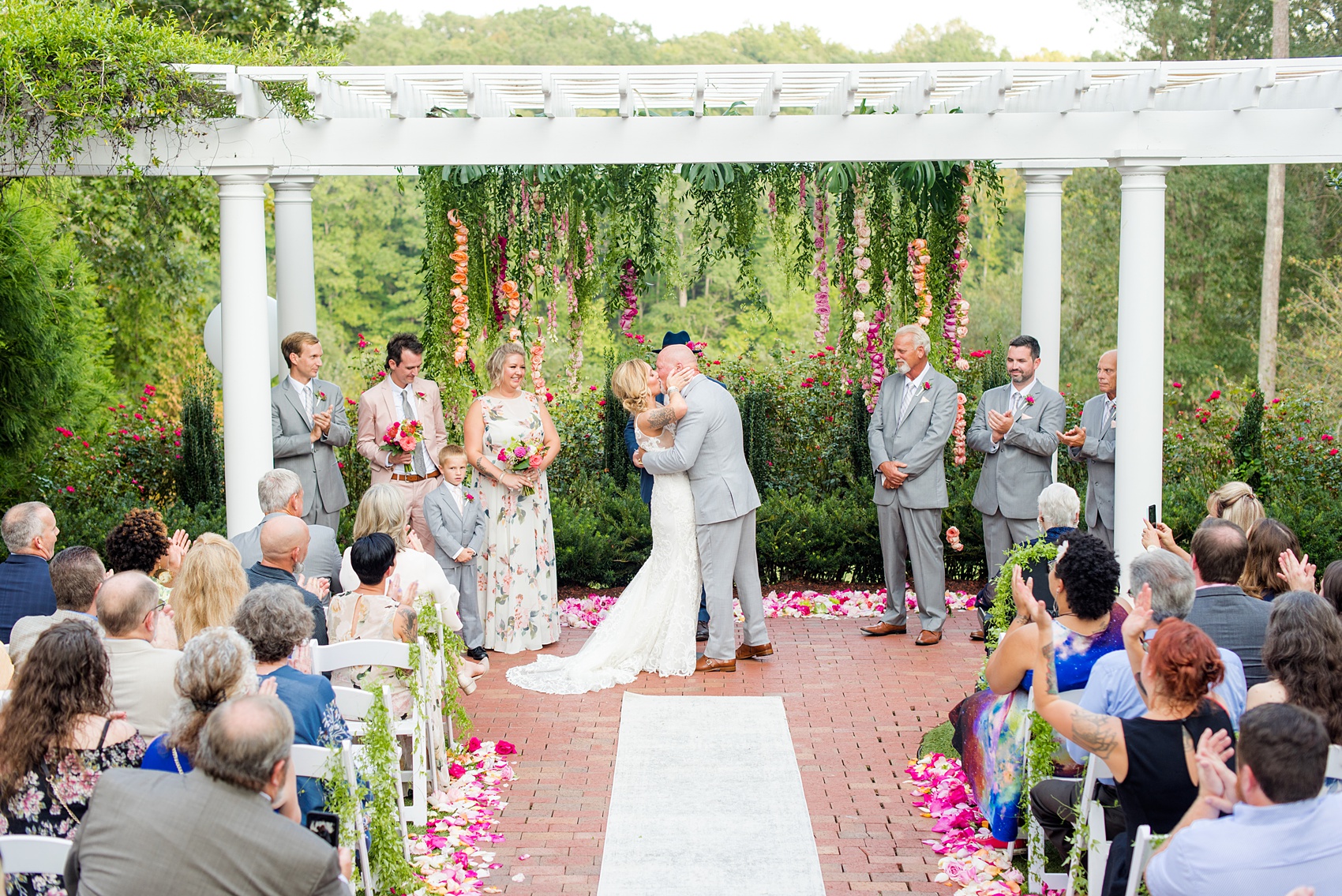 Highgrove Estate wedding photos by Mikkel Paige Photography. It’s a beautiful venue for a wedding large or small, near Raleigh, North Carolina. This wedding had fun signs, custom stationery and table numbers that said places the bride & groom travel to, and romantic candlelight planned by @asouthernsoiree. Click through to see the tropical green leaves, pink and orange flowers dripping from their outdoor ceremony space! #NorthCarolinaVenues #MikkelPaige #ASouthernSoiree #OutdoorCeremony