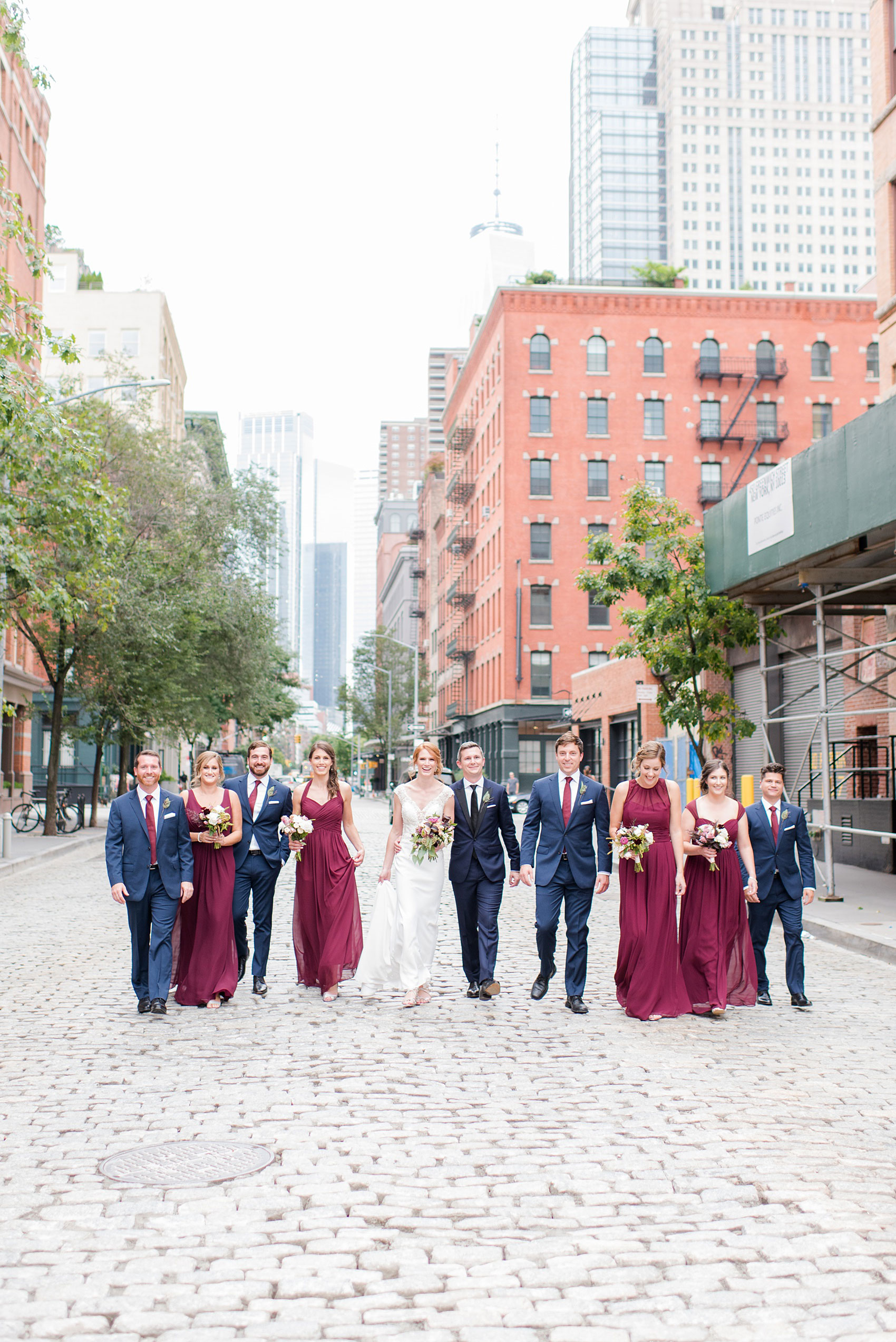 Photos of a NYC wedding venue, Tribeca Rooftop, by Mikkel Paige Photography. This ceremony and reception location has an outdoor space overlooking the Manhattan skyline. These pictures will provide inspiration in New York! The bride and groom were surrounded by bridesmaids in cranberry gowns and groomsmen in navy blue suits, holding fall flowers. Click through for more details from this celebration! #TribecaRooftop #MikkelPaige #NYCwedding #NYCWeddingVenues #NYCWeddingPhotography #FallFlowers