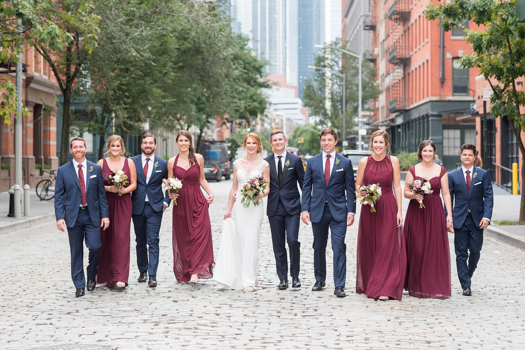 Photos of a NYC wedding venue, Tribeca Rooftop, by Mikkel Paige Photography. This ceremony and reception location has an outdoor space overlooking the Manhattan skyline. These pictures will provide inspiration in New York! The bride and groom were surrounded by bridesmaids in cranberry gowns and groomsmen in navy blue suits, holding fall flowers. Click through for more details from this celebration! #TribecaRooftop #MikkelPaige #NYCwedding #NYCWeddingVenues #NYCWeddingPhotography #FallFlowers