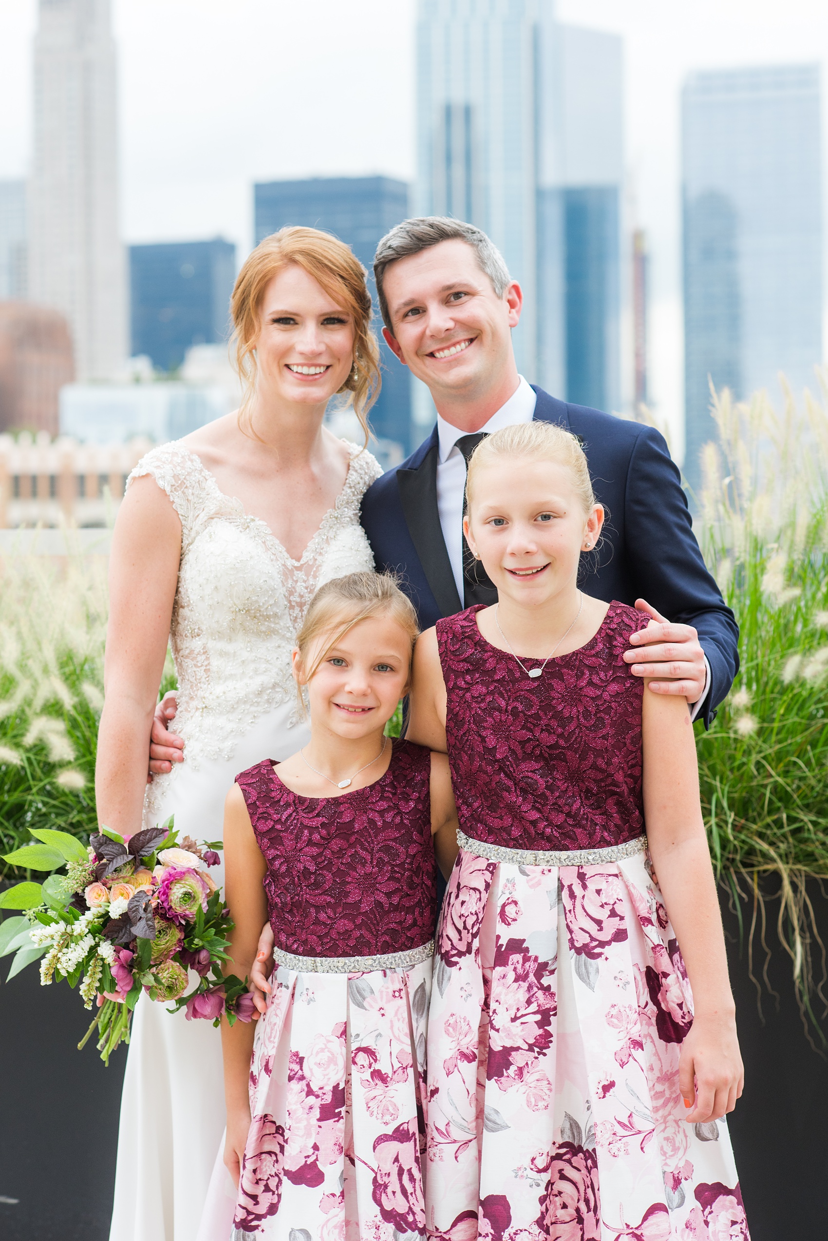 Photos of a NYC wedding venue, Tribeca Rooftop, by Mikkel Paige Photography. This ceremony and reception location has an outdoor space overlooking the Manhattan skyline. These pictures will provide inspiration in New York! The bride and groom posed for a photo with their flower girls, in complimentary cranberry patterned floral dresses. Click through for more details from this celebration! #TribecaRooftop #MikkelPaige #NYCwedding #NYCWeddingVenues #NYCWeddingPhotography #FlowerGirls