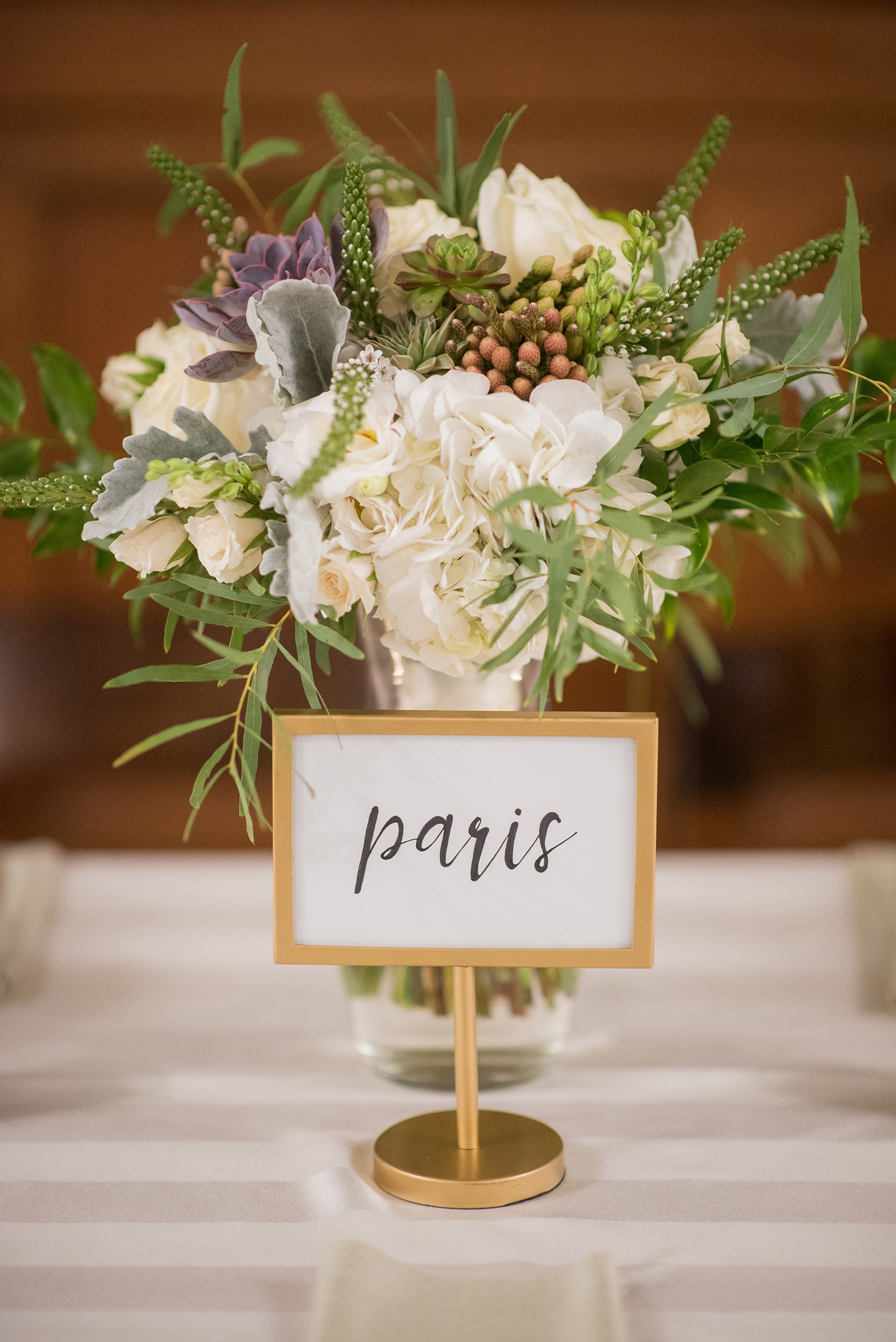 Mikkel Paige Photography captures beautiful details and fall styles during a wedding in Downtown Raleigh, North Carolina. All Saints Chapel venue was decorated with gold + silver decor and autumn accents. Custom signage was on tables at the reception with names of places the bride and groom traveled. Click through for all the event details from this celebration! #MikkelPaige #RaleighWeddingPhotographer #RaleighWedding #DowntownRaleighWedding #travelwedding #brideandgroom