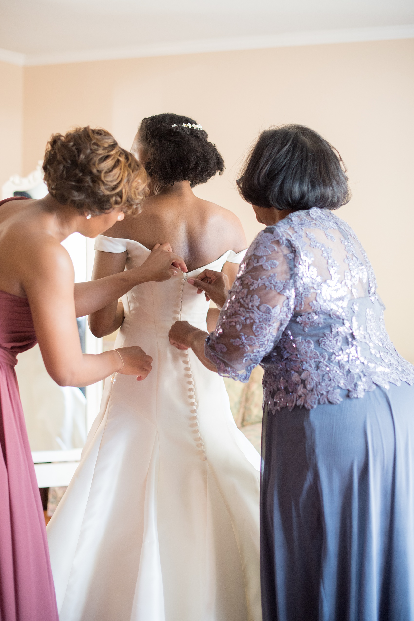 A fall wedding with burgundy, dusty rose and grey details. The bride got ready at her childhood home near the venue with her mother and sister, also the Maid of Honor, helping her into her Anne Barge, off-the-shoulder gown. Mikkel Paige Photography, photographer in Greenville NC and Raleigh captured this wedding at Rock Springs Center, planned by @vivalevent. Click through for more details and pictures! #mikkelpaige #northcarolinawedding #southernwedding #gettingready #burgundywedding