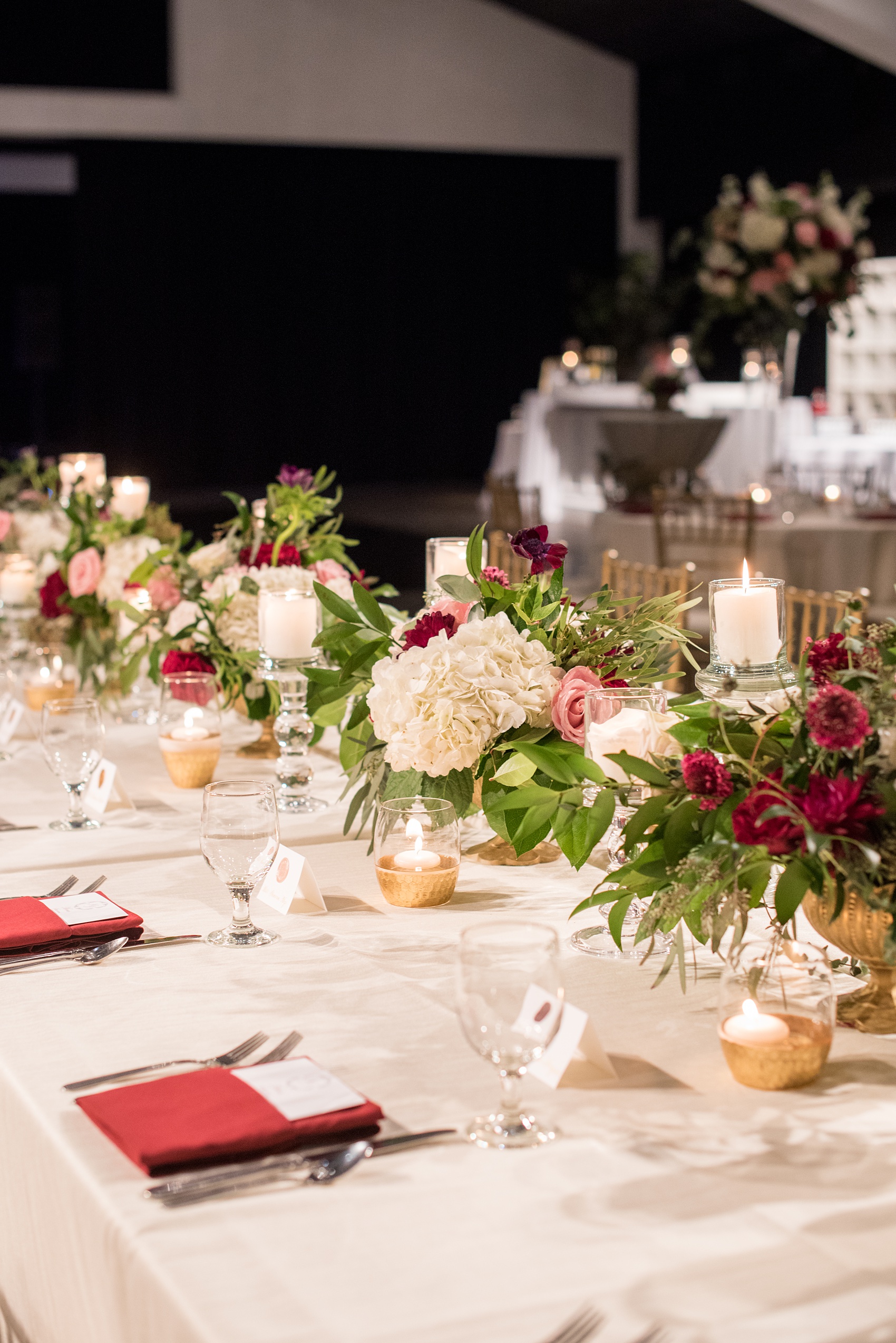 A fall wedding with burgundy, dusty rose and grey details. The reception room was filled with high + low floral centerpieces, with red and pink details, + lots of candlelight. Marble tiles served as table numbers. Mikkel Paige Photography, photographer in Greenville NC and Raleigh, captured this wedding at Rock Springs Center, planned by @vivalevent. Click through for more details and pictures from their day! #mikkelpaige #northcarolinawedding #southernwedding #weddingreception #burgundywedding