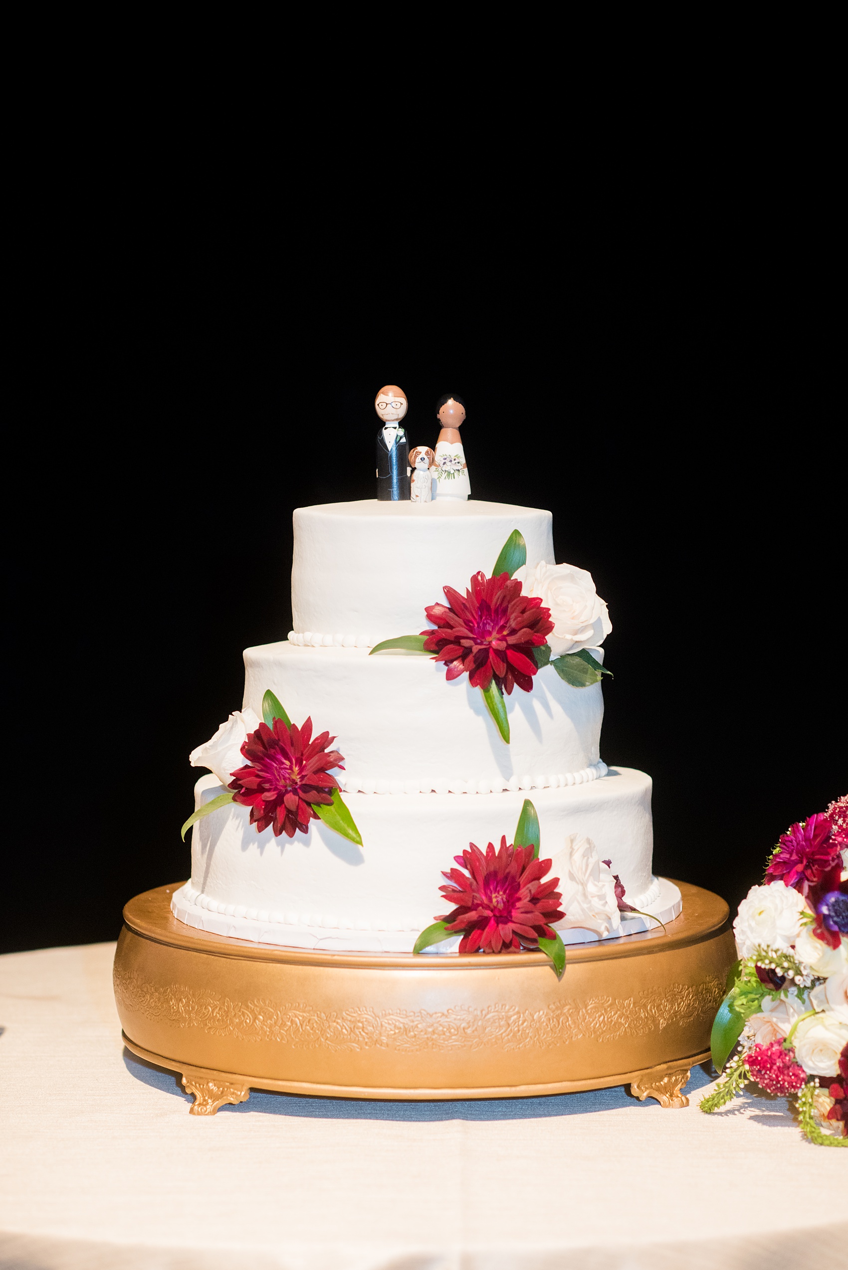 A fall wedding with burgundy, dusty rose and grey details. The couple cut their three tiered, white fondant cake with a peg figure cake topper with the bride, groom, and their dog. Mikkel Paige Photography, photographer in Greenville NC and Raleigh, captured this wedding at Rock Springs Center, planned by @vivalevent. Click through for more details and pictures from their day! #mikkelpaige NCwedding #northcarolinawedding #southernwedding #caketopper #dahlias #burgundywedding