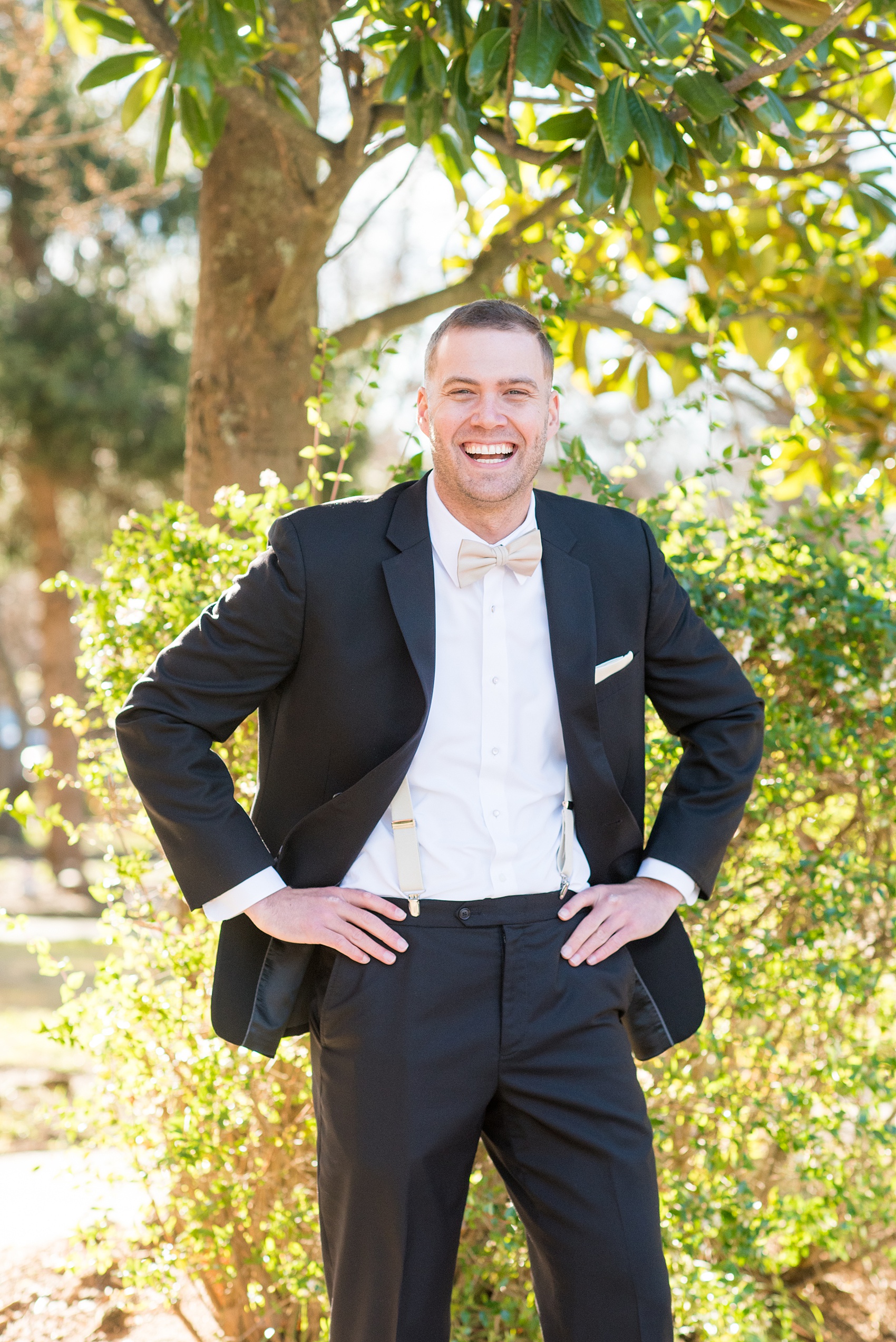 Pictures from a Christmas inspired wedding in downtown Raleigh, North Carolina by Mikkel Paige Photography. This candid laughing photo shows the groom wearing a tuxedo and tan bow tie for a winter reception at The Stockroom at 230. Click through for more ideas from their beautiful celebration, including details and decor photos in a green and gold decor palette. #mikkelpaige #raleighweddingphotographer #downtownRaleigh #christmaswedding #greenandgoldwedding #groom #holidaywedding #winterwedding