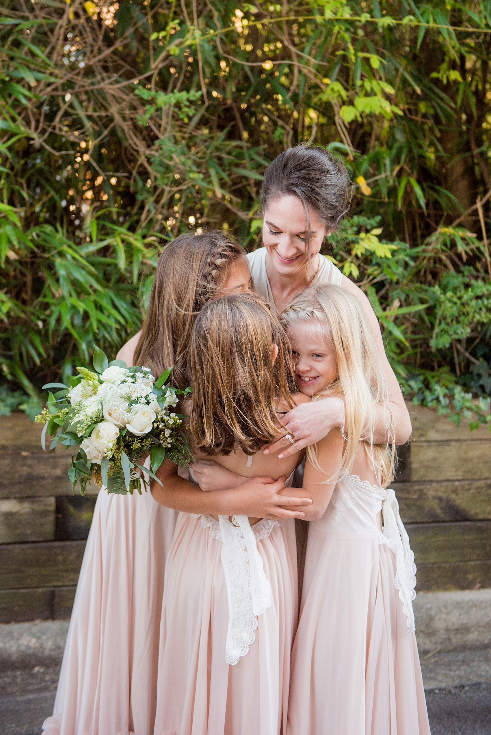 Candid pictures from a Christmas inspired wedding in downtown Raleigh, North Carolina by Mikkel Paige Photography. The bridesmaids wore mismatched pink gowns and carried white and green, holiday inspired bouquets - and one of the bridesmaids hugged the three flower girls during the cold winter weather! Click through to see more picture ideas from a beautiful celebration at The Stockroom at 230. #mikkelpaige #raleighweddingphotographer #downtownRaleigh #weddingparty #winterwedding #flowergirls