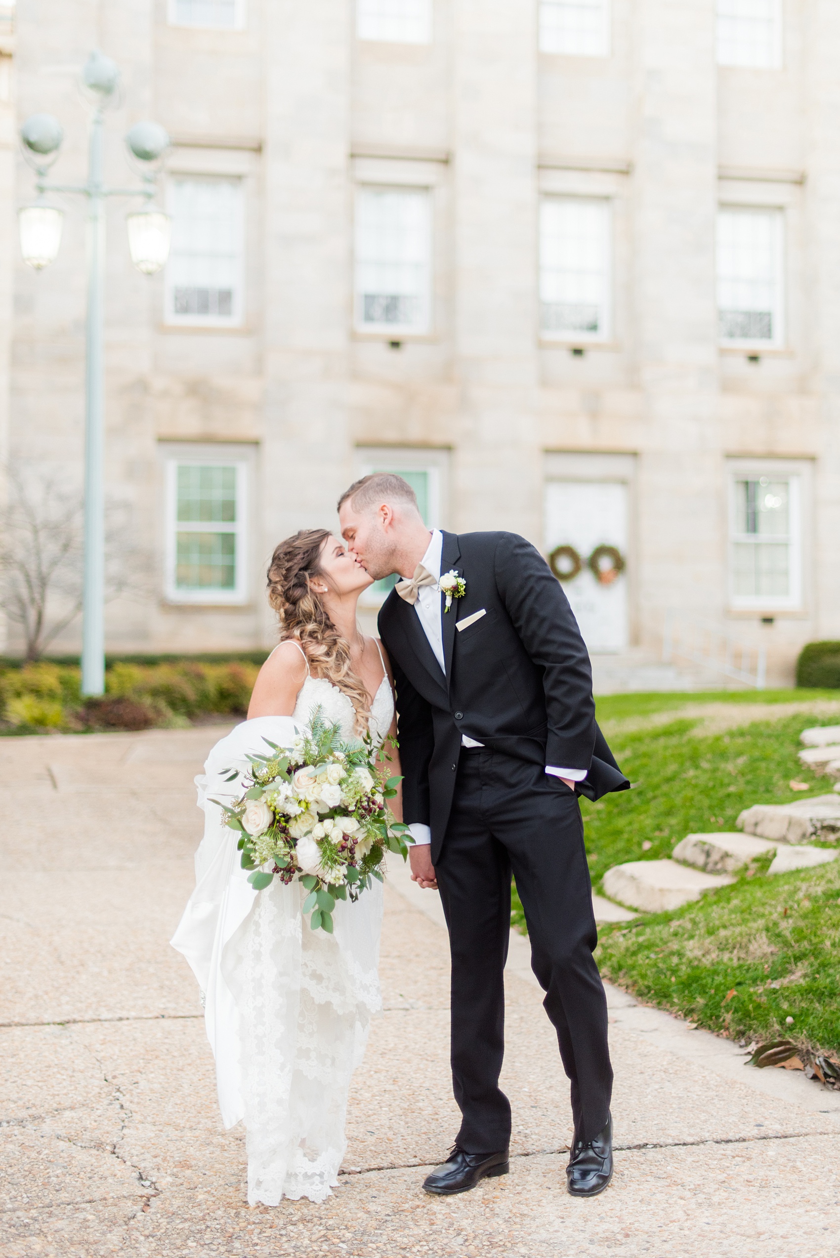 Pictures from a Christmas inspired wedding in downtown Raleigh, North Carolina by Mikkel Paige Photography. The bride and groom took outdoor portraits by the capital. She had a beautiful goddess fishtail braid hair style and lace gown. Click through for more ideas from a beautiful celebration, including details + decor photos in a green and gold decor palette for their reception. #mikkelpaige #raleighweddingphotographer #downtownRaleigh #christmaswedding #greenandgoldwedding #brideandgroom