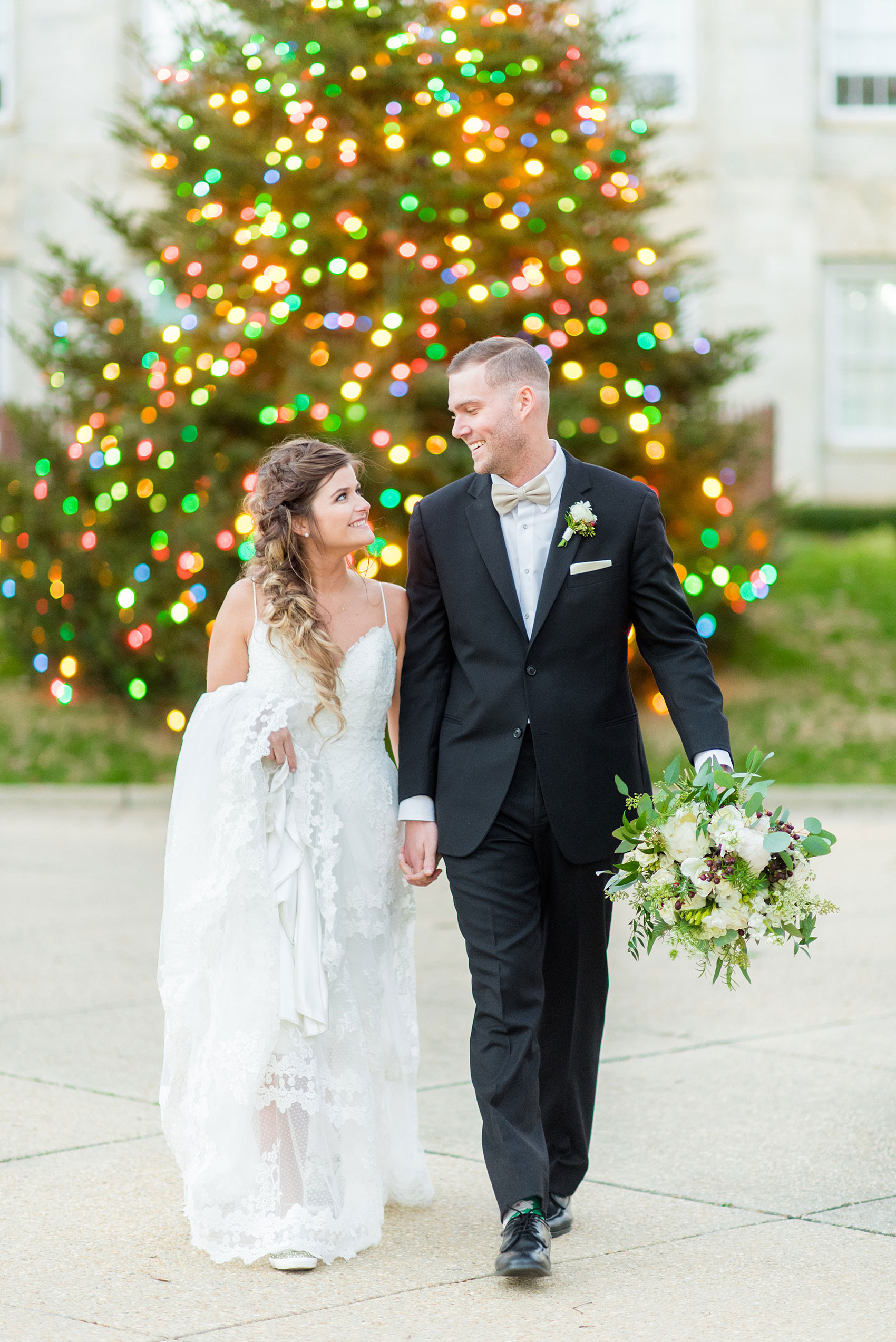 Pictures from a holiday inspired wedding in downtown Raleigh, North Carolina by Mikkel Paige Photography. The bride and groom took outdoor portraits by the capital with the Christmas lights twinkling behind them. She had a beautiful goddess fishtail braid hair style and lace gown. Click through for more ideas from a beautiful celebration, including details + decor photos in a green + gold decor palette for their reception. #mikkelpaige #raleighweddingphotographer #downtownRaleigh #brideandgroom 