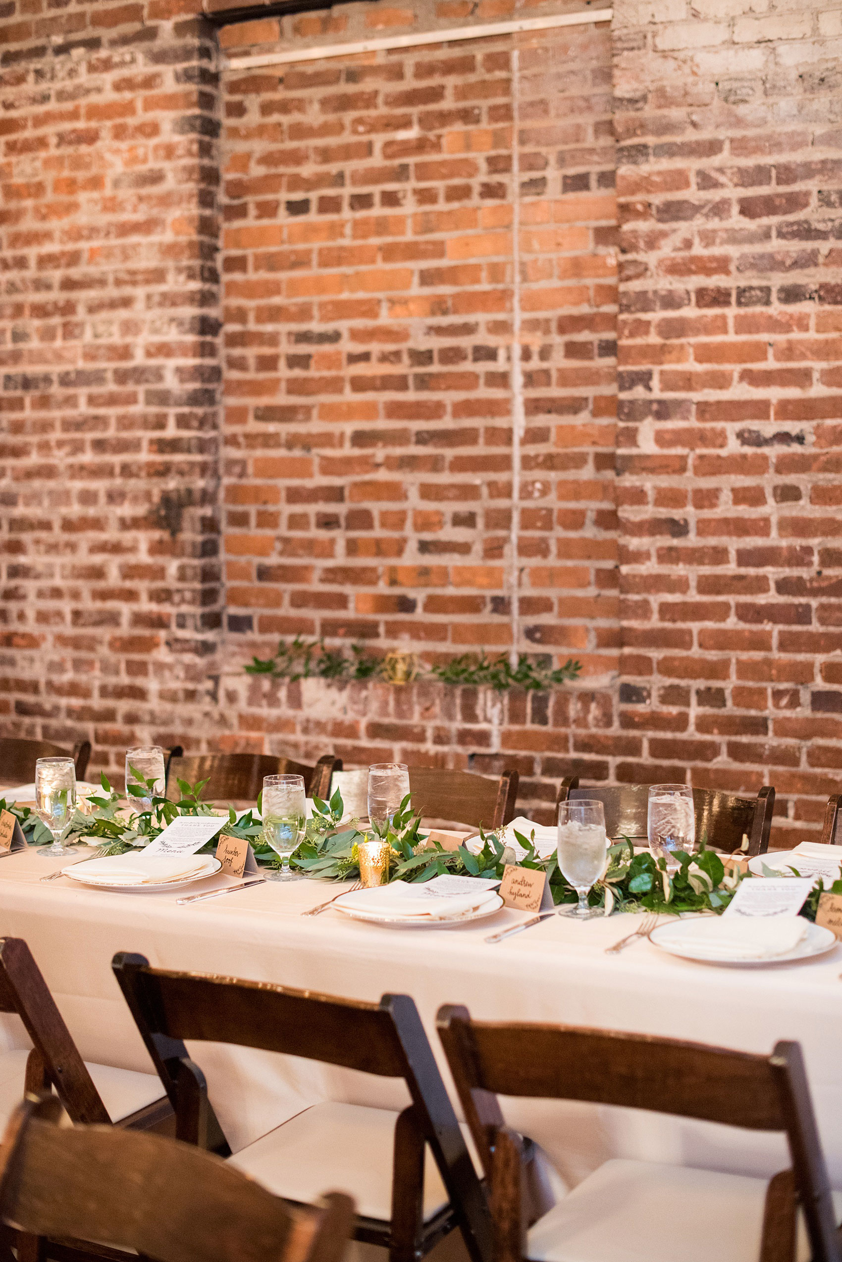 Pictures from a Christmas inspired wedding in downtown Raleigh, North Carolina by Mikkel Paige Photography. The bride and groom had a reception at the rustic venue, The Stockroom at 230, with pink linens, candlelight and greenery details. Click through for more ideas from their beautiful celebration with a pink and gold palette! #mikkelpaige #raleighweddingphotographer #downtownRaleigh #holidaywedding #ChristmasWedding #headtabledetails
