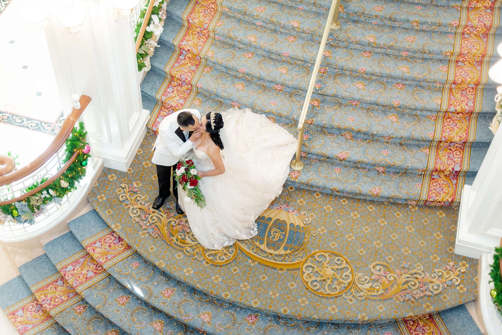 Walt Disney World photographs by Mikkel Paige Photography. The bride and groom had December pictures at the Grand Floridian Resort, Wedding Pavilion and Contemporary Hotel. It had a Beauty and the Beast theme and the bride wore a beautiful rose embroidered dress, befitting of a princess. Her red rose bouquet had holiday greenery and a cascading effect. The groom wore a white tuxedo. #disneywedding #disneybride #waltdisneyworld #DisneyWorldWedding #cascadingbouquet