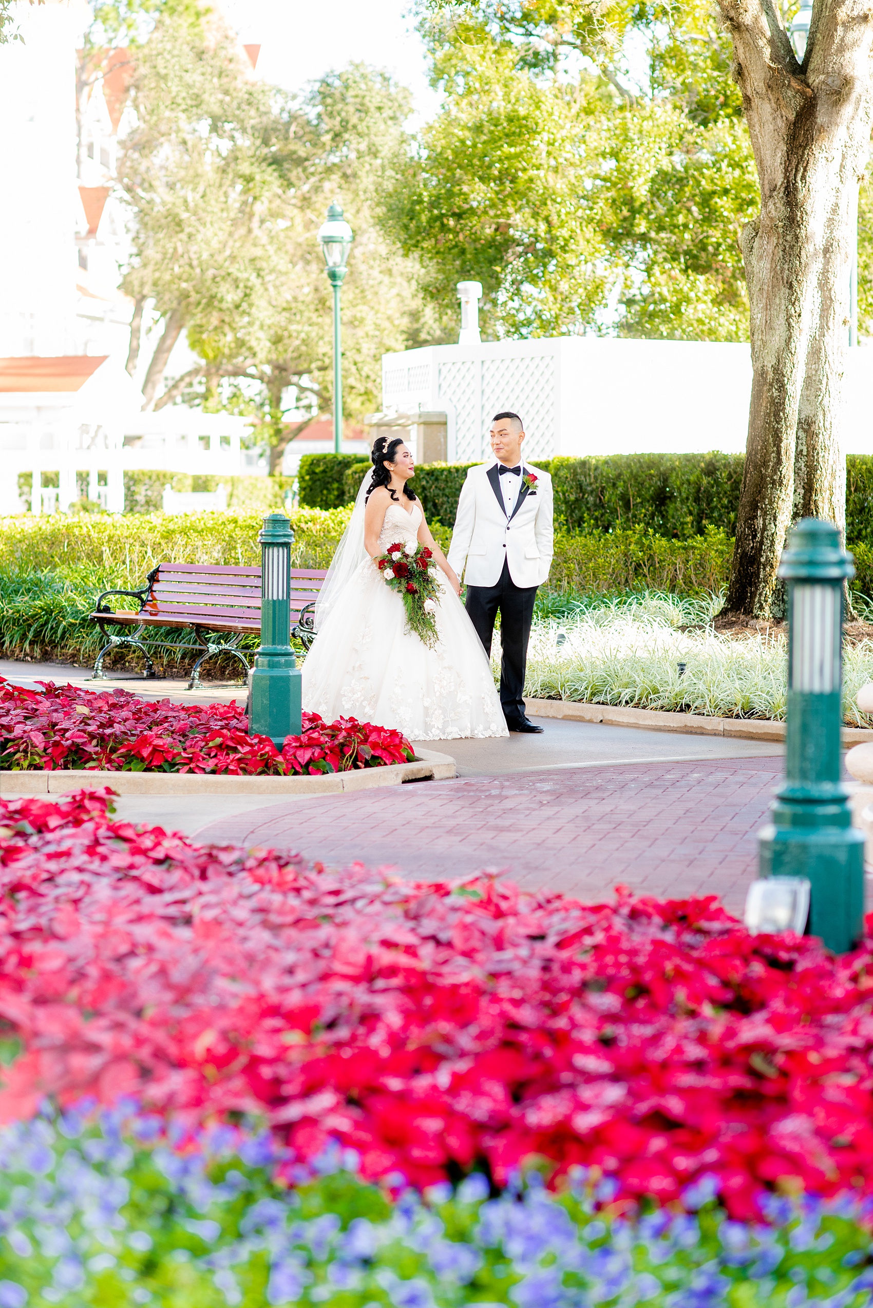 Walt Disney World photographs by Mikkel Paige Photography. The bride and groom had December pictures at the Grand Floridian Resort, Wedding Pavilion and Contemporary Hotel. It had a Beauty and the Beast theme and the bride wore a beautiful rose embroidered dress, befitting of a princess. Her red rose bouquet had holiday greenery and a cascading effect. The groom wore a white tuxedo. #disneywedding #disneybride #waltdisneyworld #DisneyWorldWedding #cascadingbouquet