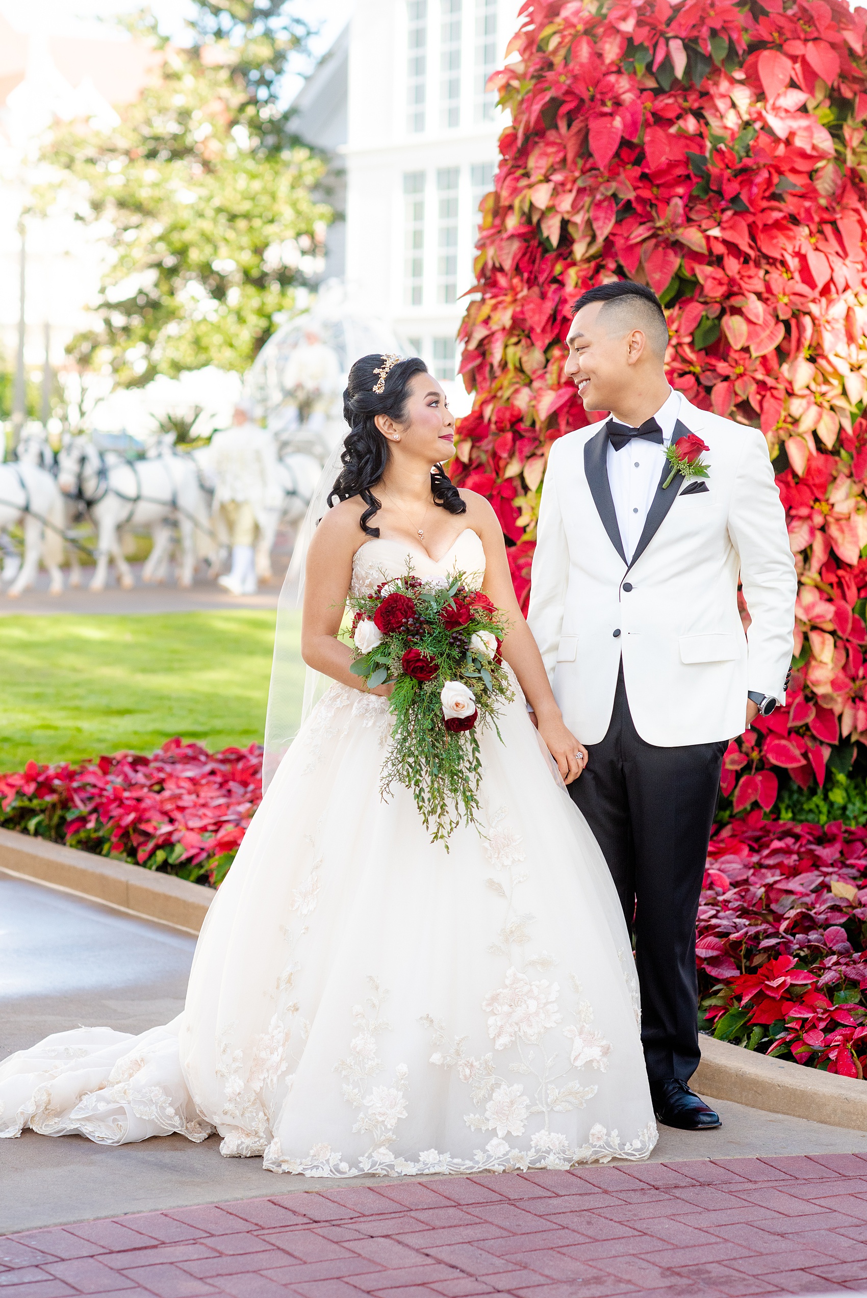 Walt Disney World photographs by Mikkel Paige Photography. The bride and groom had December pictures at the Grand Floridian Resort, Wedding Pavilion and Contemporary Hotel. It had a Beauty and the Beast theme and the bride wore a beautiful rose embroidered dress, befitting of a princess. Her red rose bouquet had holiday greenery and a cascading effect. The groom wore a white tuxedo. #disneywedding #disneybride #waltdisneyworld #DisneyWorldWedding #cascadingbouquet