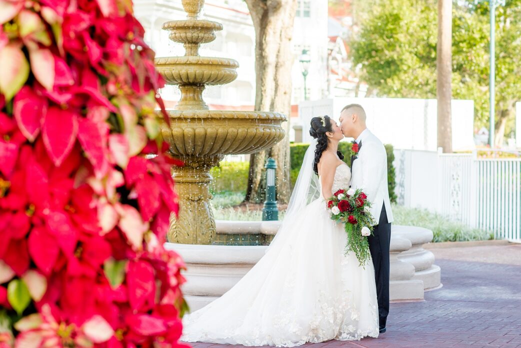 Walt Disney World photographs by Mikkel Paige Photography. The bride and groom had December pictures at the Grand Floridian Resort, Wedding Pavilion and Contemporary Hotel. It had a Beauty and the Beast theme and the bride wore a beautiful rose embroidered dress, befitting of a princess. Her red rose bouquet had holiday greenery and a cascading effect. The groom wore a white tuxedo. #disneywedding #disneybride #waltdisneyworld #DisneyWorldWedding #cascadingbouquet