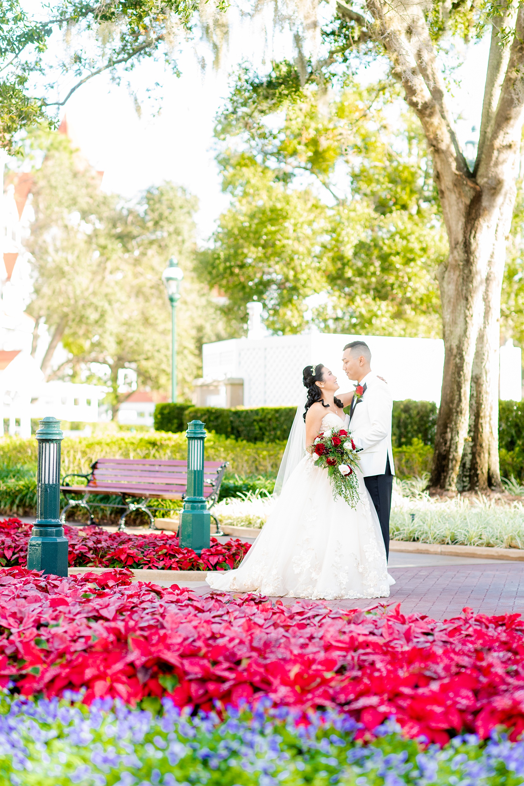 Walt Disney World photographs by Mikkel Paige Photography. The bride and groom had December pictures at the Grand Floridian Resort, Wedding Pavilion and Contemporary Hotel. It had a Beauty and the Beast theme and the bride wore a beautiful rose embroidered dress, befitting of a princess. Her red rose bouquet had holiday greenery and a cascading effect. The groom wore a white tuxedo. #disneywedding #disneybride #waltdisneyworld #DisneyWorldWedding #cascadingbouquet 