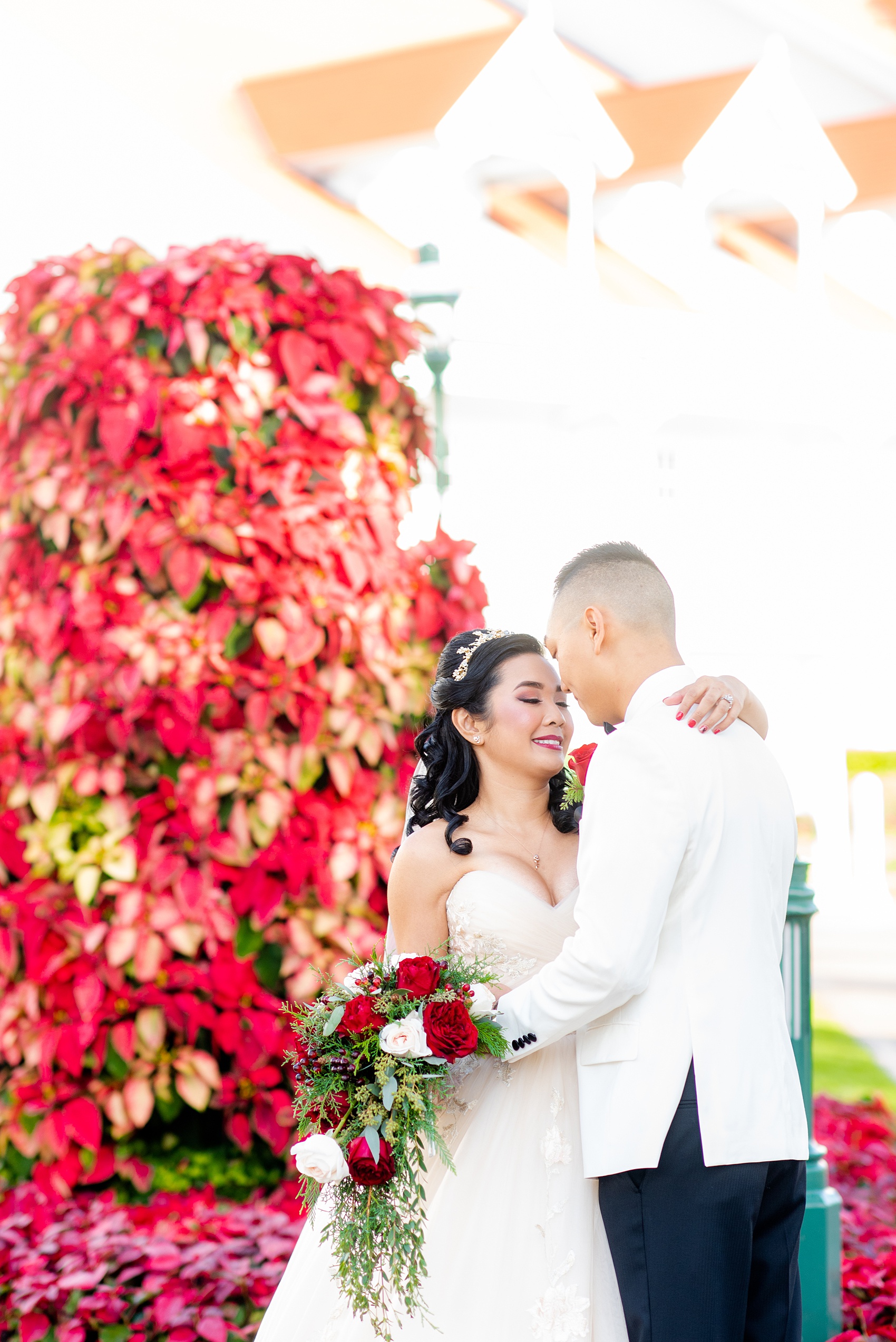 Walt Disney World photographs by Mikkel Paige Photography. The bride and groom had December pictures at the Grand Floridian Resort, Wedding Pavilion and Contemporary Hotel. It had a Beauty and the Beast theme and the bride wore a beautiful rose embroidered dress, befitting of a princess. Her red rose bouquet had holiday greenery and a cascading effect. The groom wore a white tuxedo. #disneywedding #disneybride #waltdisneyworld #DisneyWorldWedding #cascadingbouquet