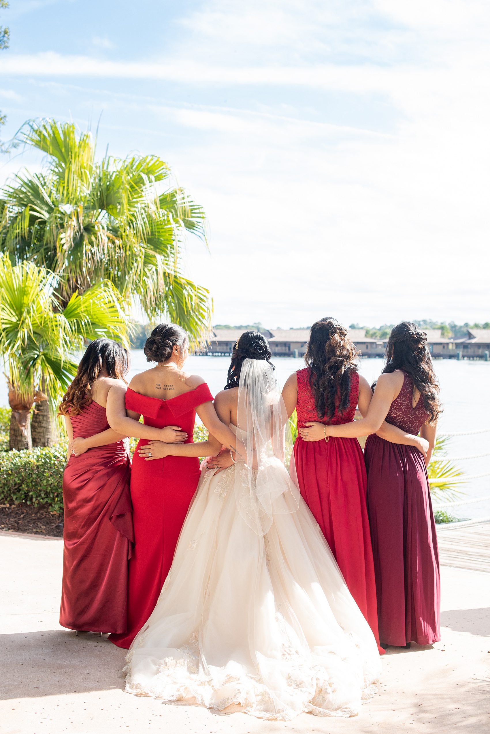 Photographs of a Walt Disney World bridal party by Mikkel Paige Photography. The bride chose the venues of the Grand Floridian, Wedding Pavilion and The Contemporary Resort for photos and fun locations. One even overlooked the Magic Kingdom Park! Their dream wedding included red details: the bridesmaids wore mismatched dresses and carried rose bouquets. #disneywedding #disneybride #waltdisneyworld #DisneyWorldWedding #BeautyandtheBeast #redrosewedding