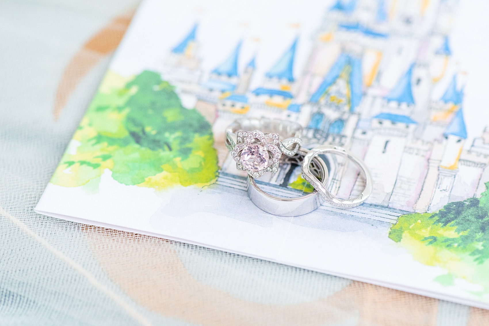 Photographs of a Walt Disney World wedding by Mikkel Paige Photography. The bride’s engagement ring was themed to Beauty and the Beast with a pink morganite center stone. It perfectly matched their invitations with Cinderella Castle as the main watercolor and the movie glass rose dome on the RSVP card. #disneywedding #disneybride #waltdisneyworld #DisneyWorldWedding #morganitering #pinkengagementring #rosering #BeautyandtheBeast