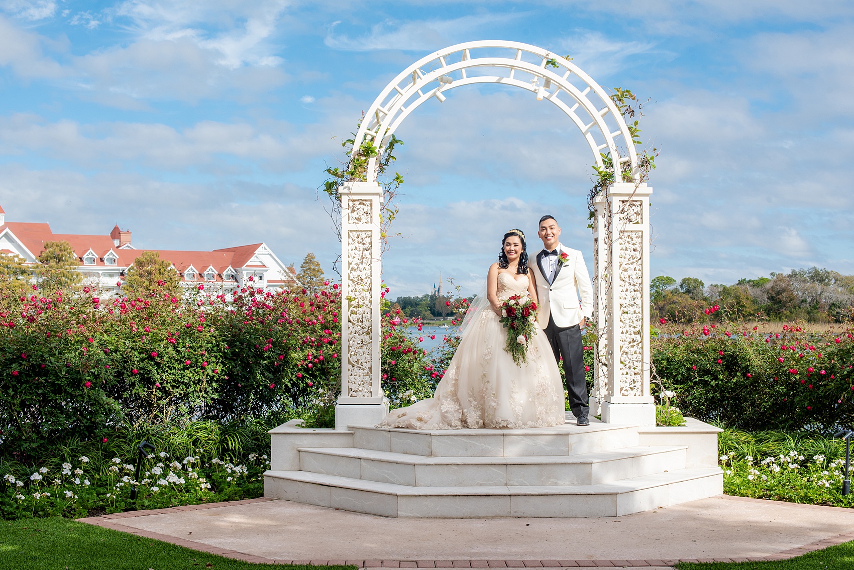 Walt Disney World photographs by Mikkel Paige Photography. The bride and groom had December pictures at the Grand Floridian Resort, Wedding Pavilion and Contemporary Hotel. It had a Beauty and the Beast theme and the bride wore a beautiful rose embroidered dress, befitting of a princess. Her red rose bouquet had holiday greenery and a cascading effect. The groom wore a white tuxedo. #disneywedding #disneybride #waltdisneyworld #DisneyWorldWedding #cascadingbouquet