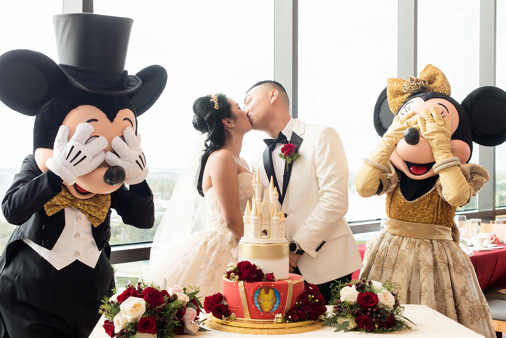 Photographs of a Walt Disney World wedding by Mikkel Paige Photography. The bride and groom had cake cutting help from Mickey Mouse and Minnie Mouse in formal attire! Their reception venue at The Contemporary Resort’s California Grill was great for fun, awesome photos with them. It overlooked the Magic Kingdom Park and Cinderella Castle! Their small, dream day included red rose details and a Beauty and the Beast theme. #disneywedding #DisneyWorldWedding #BeautyandtheBeast #MickeyandMinnie