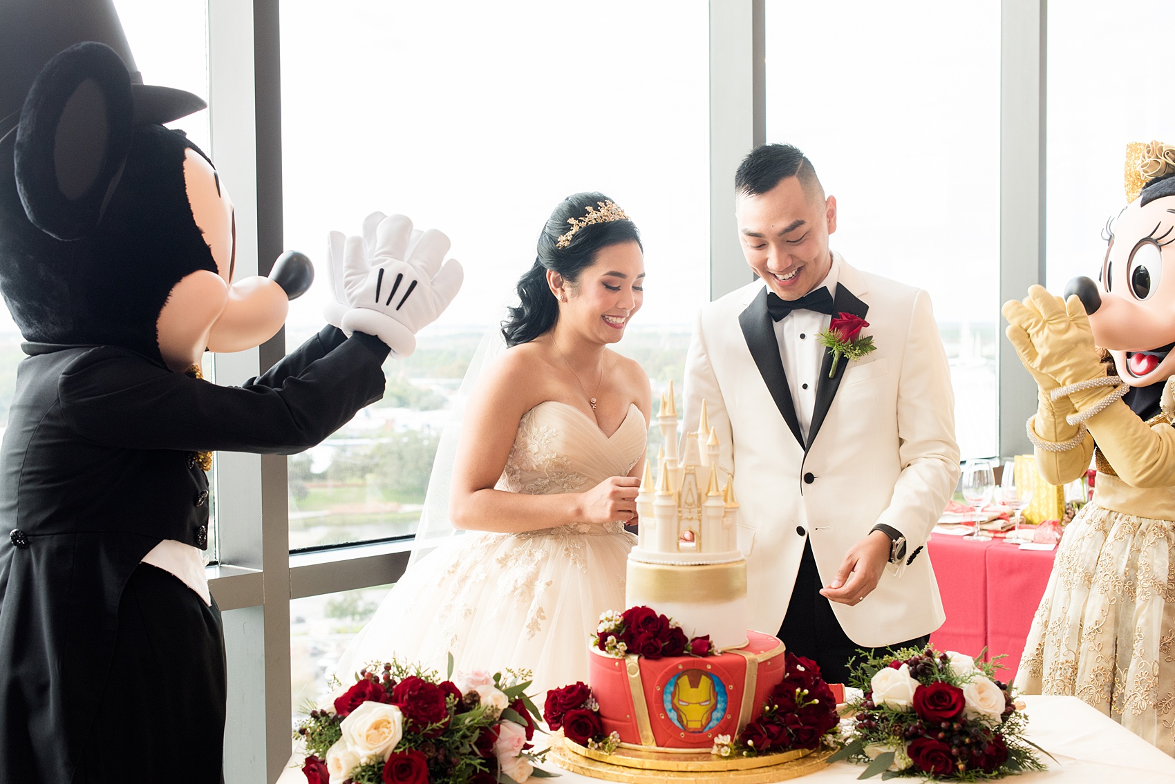 Photographs of a Walt Disney World wedding by Mikkel Paige Photography. The bride and groom had cake cutting help from Mickey Mouse and Minnie Mouse in formal attire! Their reception venue at The Contemporary Resort’s California Grill was great for fun, awesome photos with them. It overlooked the Magic Kingdom Park and Cinderella Castle! Their small, dream day included red rose details and a Beauty and the Beast theme. #disneywedding #DisneyWorldWedding #BeautyandtheBeast #MickeyandMinnie