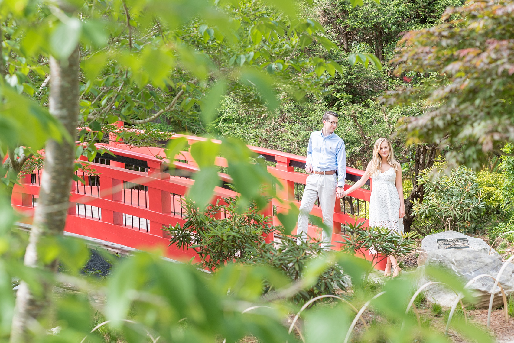 Duke Gardens engagement photos in Durham, North Carolina, by Mikkel Paige Photography. Trees with leaves in full bloom during spring reveal themselves for a May session. #DurhamPhotographer #DurhamWeddingPhotographer #SarahPDukeGardens #DukeGardens #DurhamEngagementSession #JapaneseBridge #redbridge