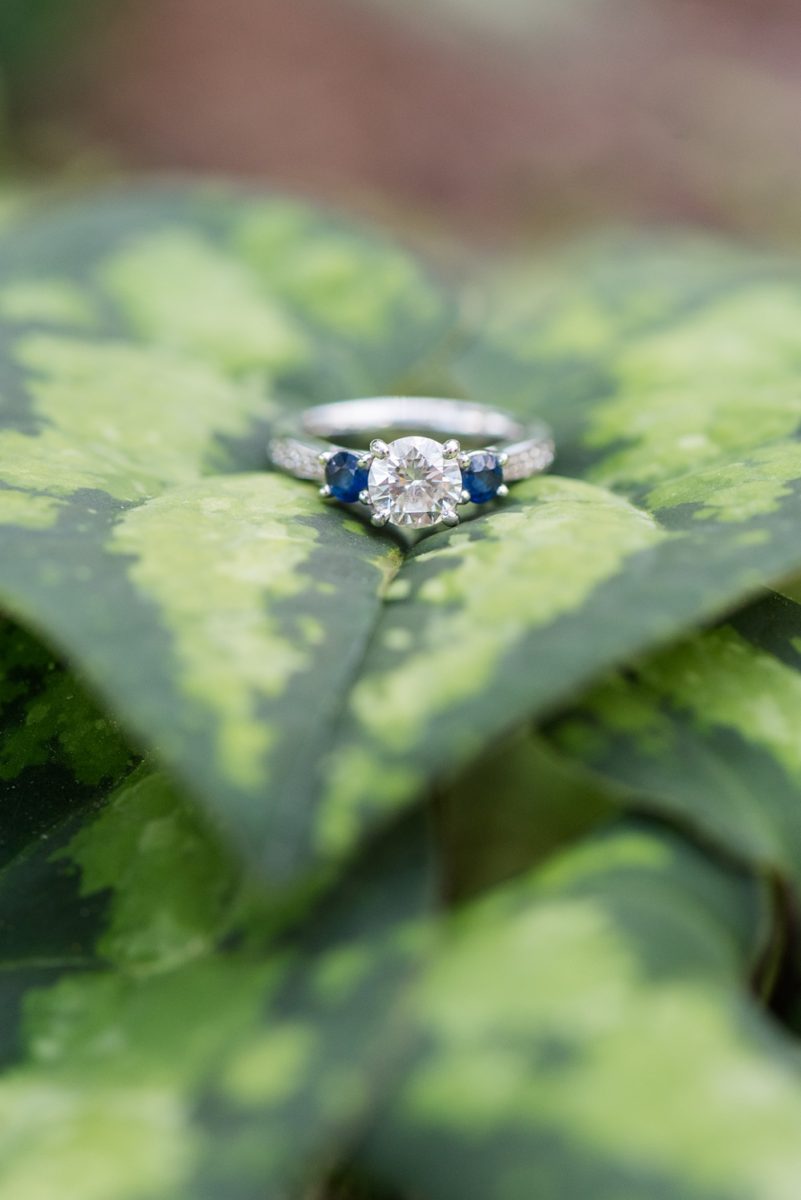 Raleigh engagement photos with murals and spring flowers in the downtown area by Mikkel Paige Photography. The bride and groom choose JC Raulston Arboretum and the Marbles Kids Museum mural for their pictures. There was a special detail of a tiny sapphire in the bride's engagement ring. #DowntownRaleigh #RaleighWeddingPhotographer #mikkelpaige #RaleighPhotographer #RaleighPhotos #RaleighNC #NorthCarolinaPhotographer #sapphireengagementring