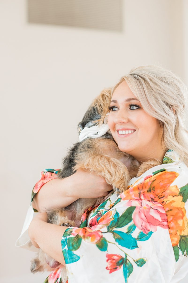 A beautiful spring wedding in Raleigh, North Carolina, at the event venue, The Stockroom at 230 and The Glass Box. Pictures of the bride getting ready with her yorkie dog by their photographer, Mikkel Paige Photography. Their hot pink and aqua colors were perfect for May as the bridesmaids celebrated with a champagne toast in floral robes. #MikkelPaige #DowntownRaleigh #RaleighWedding #RaleighVenue #TheStockroomat230 #bridesmaidsrobes #weddinggettingready