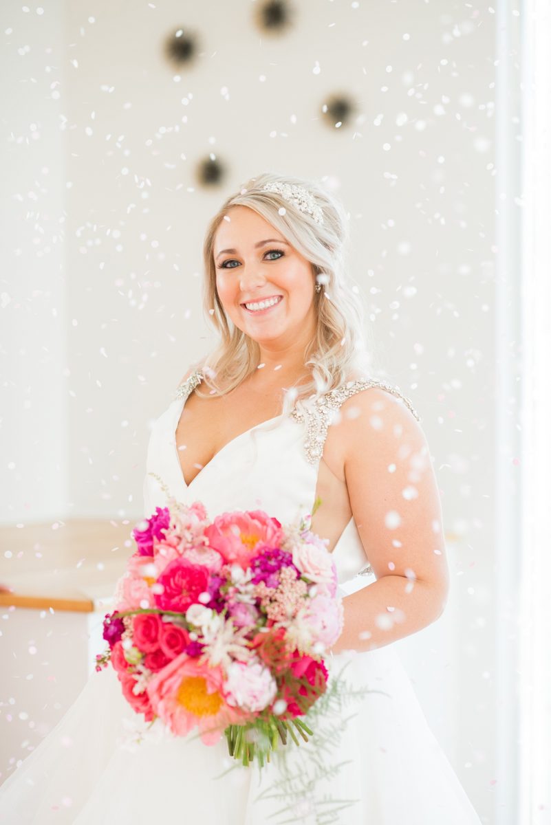 Bridesmaids celebrate with a confetti toss at The Glass Box in downtown Raleigh, North Carolina. The event venue, The Stockroom at 230 was the perfect place for a North Carolina bride and groom to get married. #MikkelPaige #DowntownRaleigh #RaleighWedding #RaleighVenue #TheStockroomat230 #theglassbox #confettiweddingphotos #confetti #weddingparty #bridesmaids #hotpinkbouquet #peonybouquet