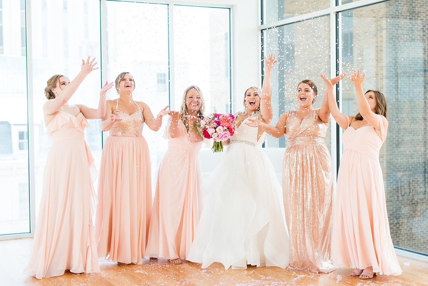 Bridesmaids celebrate with a confetti toss at The Glass Box in downtown Raleigh, North Carolina. The event venue, The Stockroom at 230 was the perfect place for a North Carolina bride and groom to get married. #MikkelPaige #DowntownRaleigh #RaleighWedding #RaleighVenue #TheStockroomat230 #theglassbox #confettiweddingphotos #confetti #weddingparty #bridesmaids