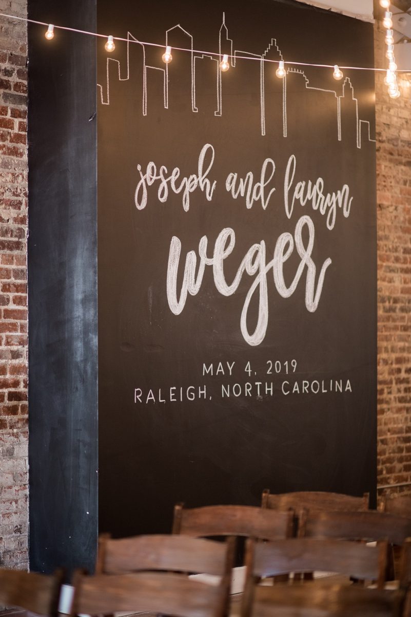 Indoor spring wedding ceremony at the event venue The Stockroom at 230 in Raleigh, North Carolina. Their photographer, Mikkel Paige Photography, captured the bride and groom’s vows in this historic building near the capital downtown. #MikkelPaige #DowntownRaleigh #RaleighWedding #RaleighVenue #TheStockroomat230 #weddingceremony #indoorweddingceremony #chalkboardwall