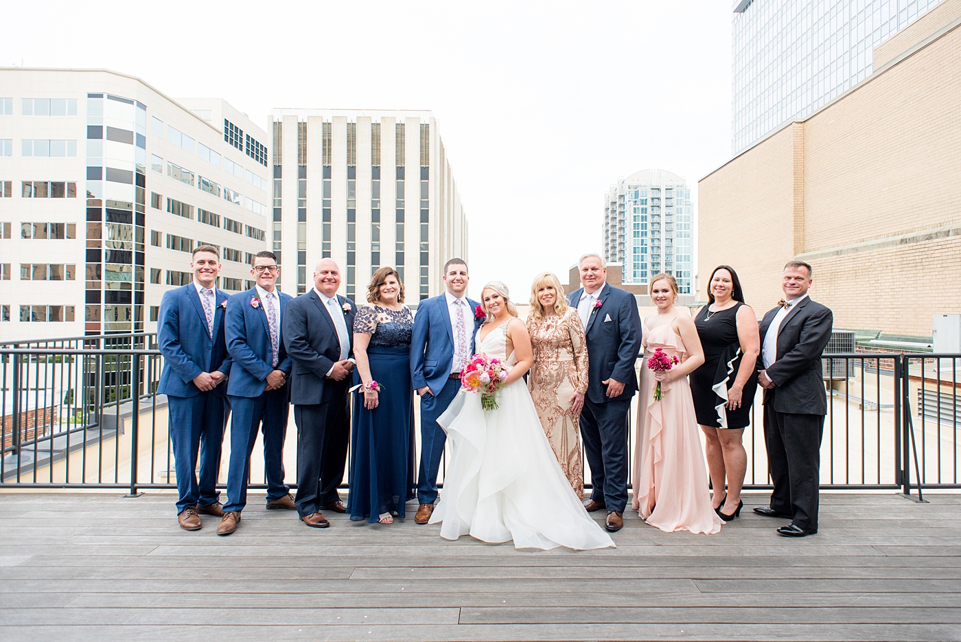 Raleigh wedding photographer, Mikkel Paige Photography, pictures of mismatched pink bridesmaids + groomsmen in blue suits with floral ties in downtown Raleigh, North Carolina at the event venue The Stockroom at 230, The Glass Box, and capital building. Their hot pink peony + carnation bouquets were perfect for a spring May celebration. #MikkelPaige #DowntownRaleigh #RaleighWedding #RaleighVenue #TheStockroomat230 #capitalcity #peonies #carnations #pinkbridesmaids #bridalpartyphotos #weddingparty