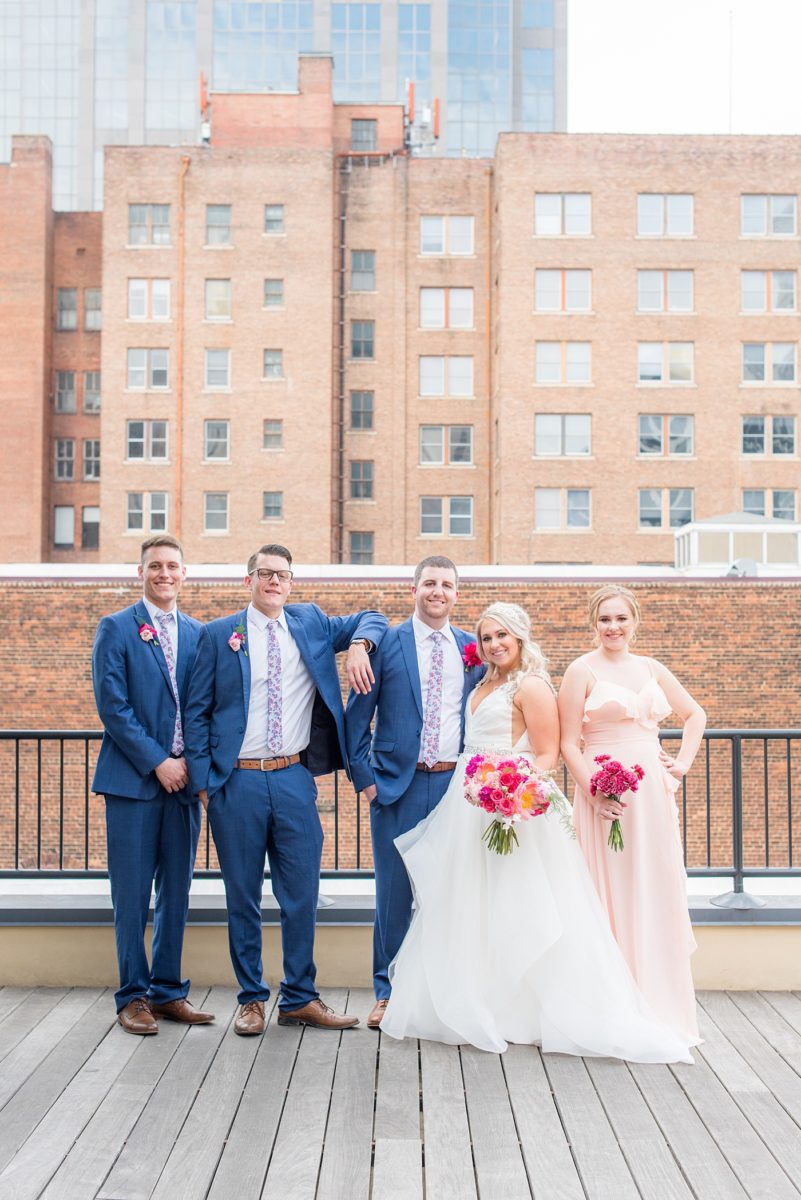 Raleigh wedding photographer, Mikkel Paige Photography, pictures of mismatched pink bridesmaids + groomsmen in blue suits with floral ties in downtown Raleigh, North Carolina at the event venue The Stockroom at 230, The Glass Box, and capital building. Their hot pink peony + carnation bouquets were perfect for a spring May celebration. #MikkelPaige #DowntownRaleigh #RaleighWedding #RaleighVenue #TheStockroomat230 #capitalcity #peonies #carnations #pinkbridesmaids #bridalpartyphotos #weddingparty