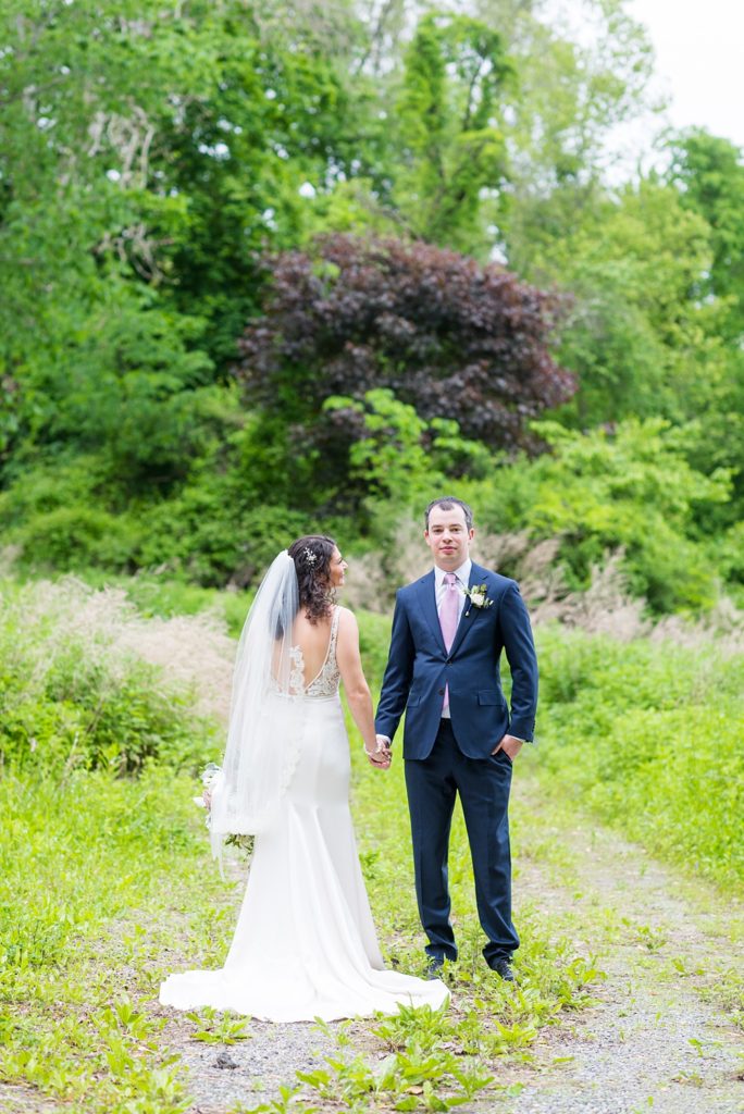 Westchester wedding photography at a beautiful outdoor and indoor venue called Crabtree's Kittle House. Photos by Mikkel Paige Photography. The bride and groom looked classic in a blue suit and v-neck summer lace gown with a deep back. They had a bouquet and boutonniere with poppy pods, scabiosas and roses in a purple + green palette. #mikkelpaige #westchestervenue #westchesterphotography #crabtreeskittlehouse #bridestyle #Maywedding #brideandgroom