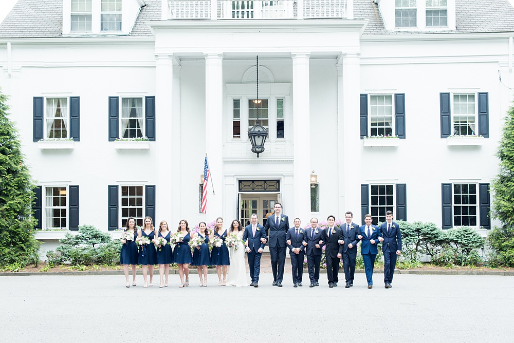 Westchester wedding photography at a beautiful outdoor and indoor venue called Crabtree's Kittle House. Photos by Mikkel Paige Photography. The bridesmaids wore midnight navy short dresses + groomsmen blue suits with mismatched boutonnieres + bouquets in purple and green with poppy pods, scabiosa pods, roses and eucalyptus by Denise Fasanello for a May Memorial Day Weekend celebration. #mikkelpaige #westchestervenue #westchesterphotography #crabtreeskittlehouse #bridalparty #bluebridesmaids