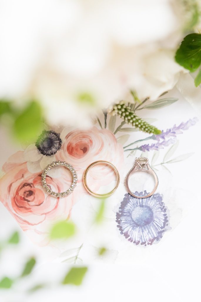 Westchester wedding photography at a beautiful outdoor and indoor venue called Crabtree's Kittle House. Photos by Mikkel Paige Photography. This detail photo shows the bride and groom's diamond and gold wedding bands with their flowers and watercolor invitation envelope liner. #mikkelpaige #westchestervenue #westchesterphotography #crabtreeskittlehouse #summerwedding #weddingrings #diamondring