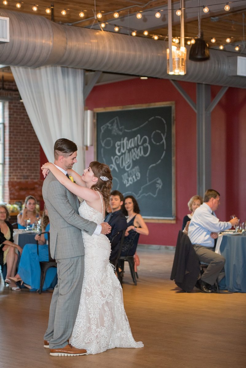 Pictures at a Durham, North Carolina wedding venue by Mikkel Paige Photography. The Rickhouse was the perfect outdoor/indoor space for the bride and groom's celebration. The couple chose fun yellow and blue colors for their summer decor and danced a romantic first dance in this reception photo. #mikkelpaige #therickhouse #durhamweddingphotos #durhamwedding #northcarolinaweddingphotographer #durhamweddingphotographer #firstdance